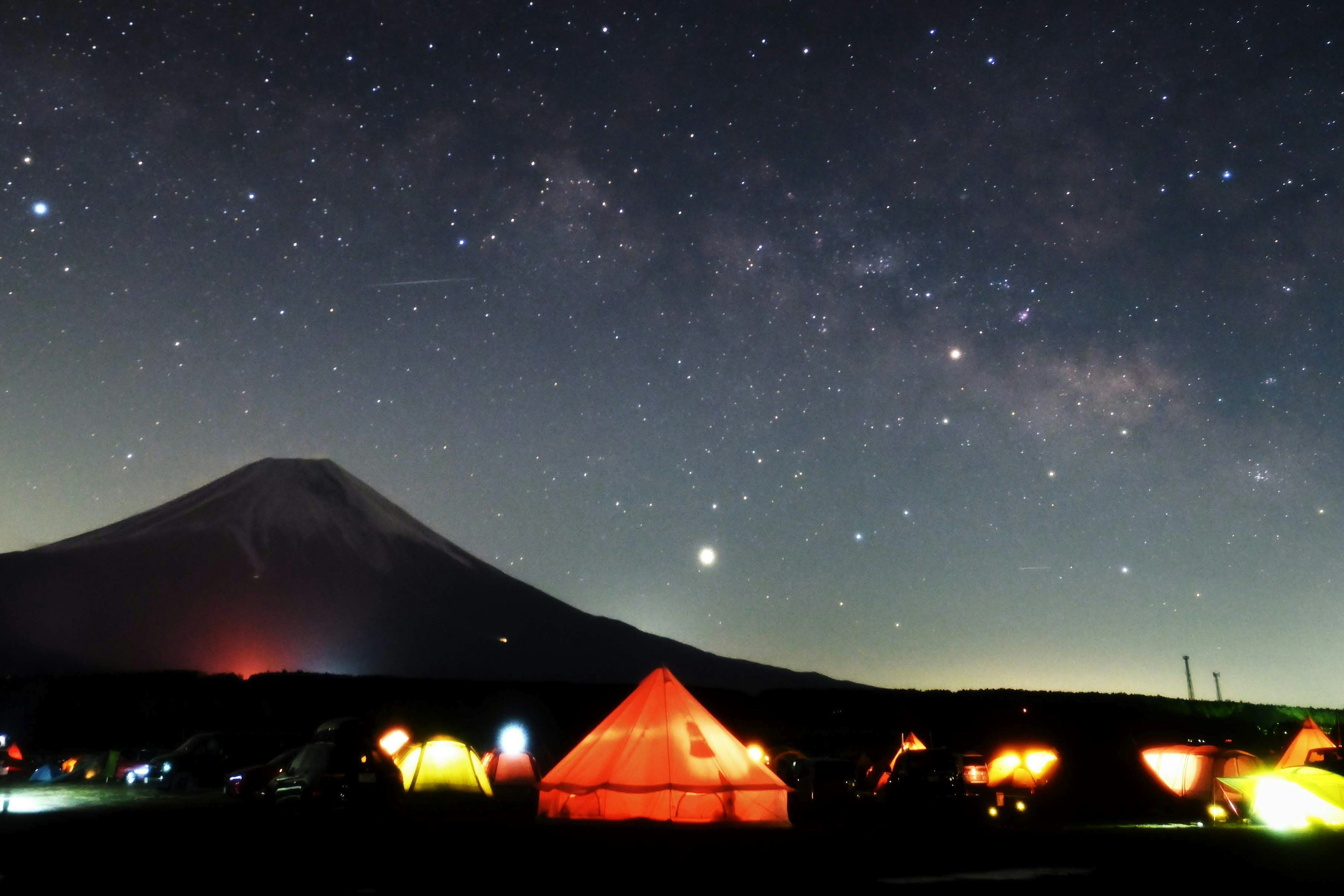 Sitio de campamento bajo un cielo estrellado con el monte Fuji al fondo