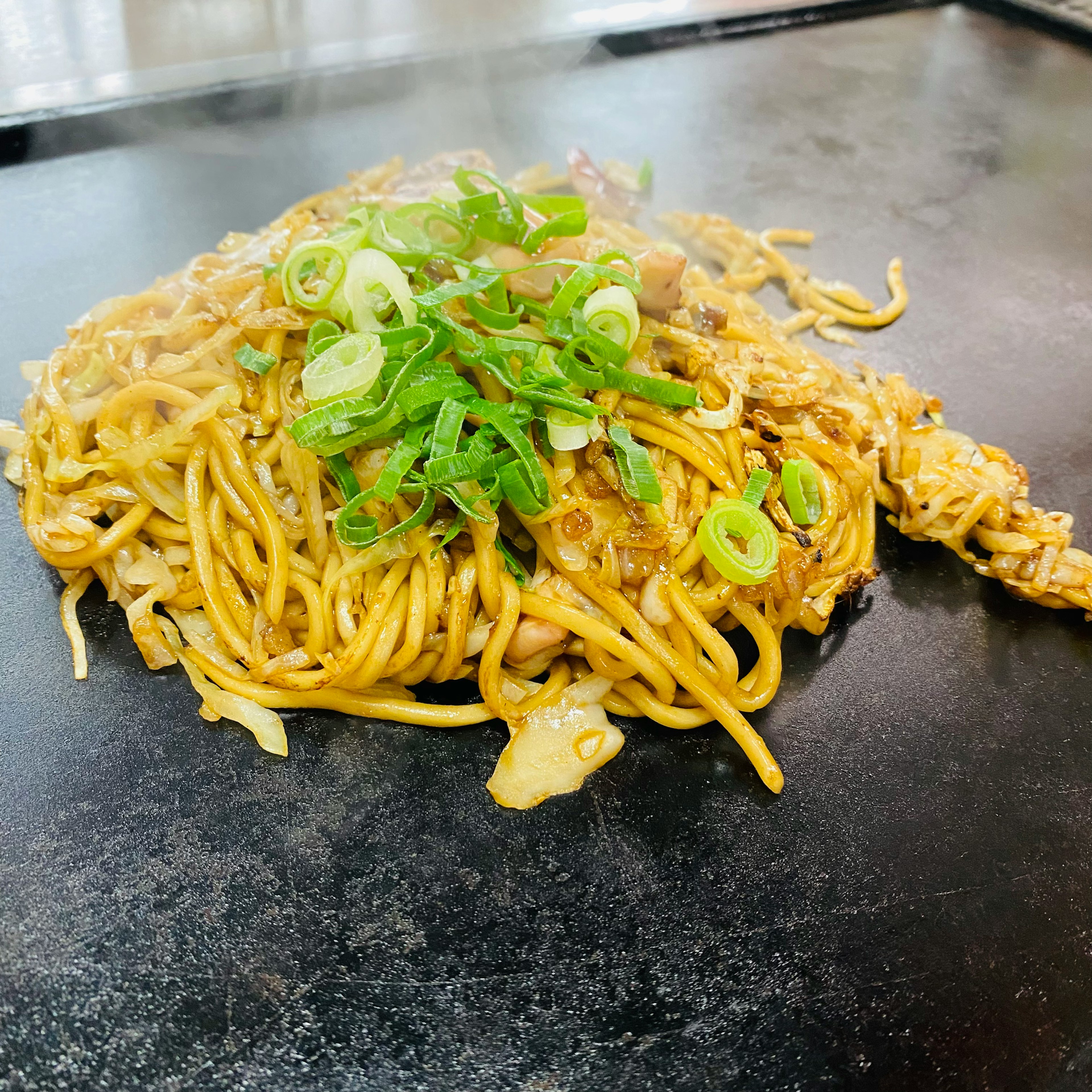 Stir-fried noodles topped with green onions on a hot plate