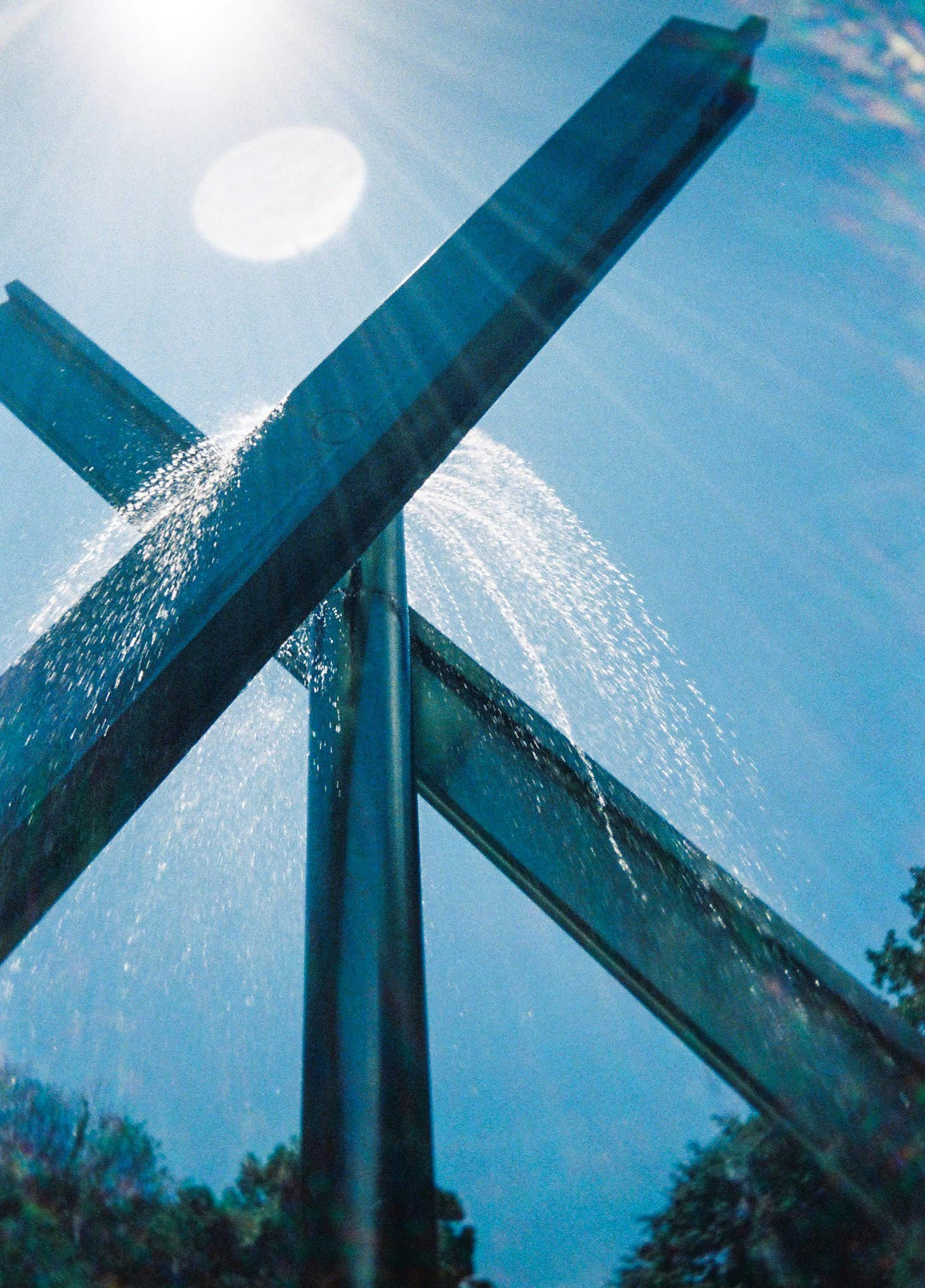 Escultura de metal con agua rociando bajo un cielo azul claro