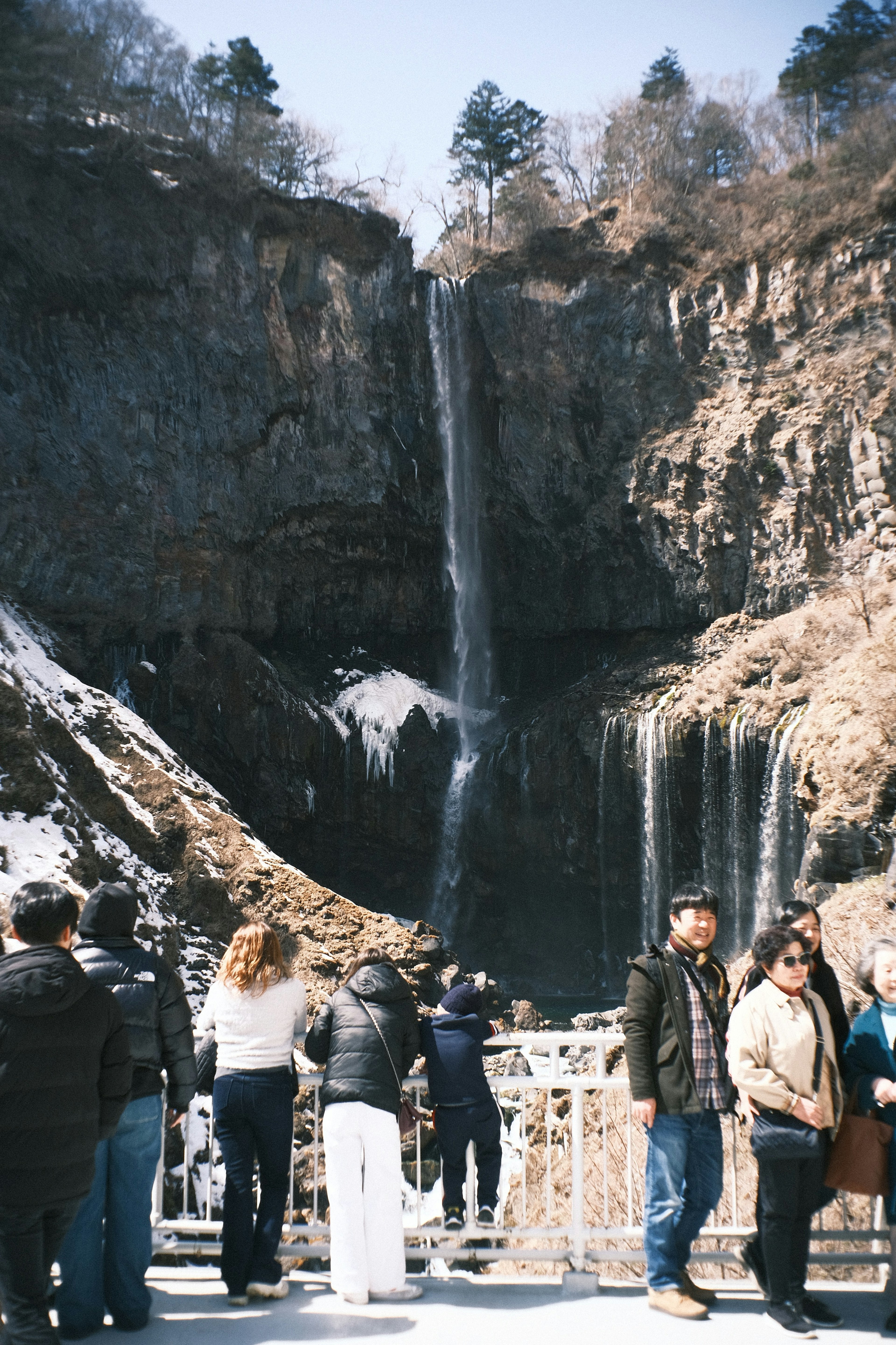 Turisti in piedi davanti a una cascata in un paesaggio invernale