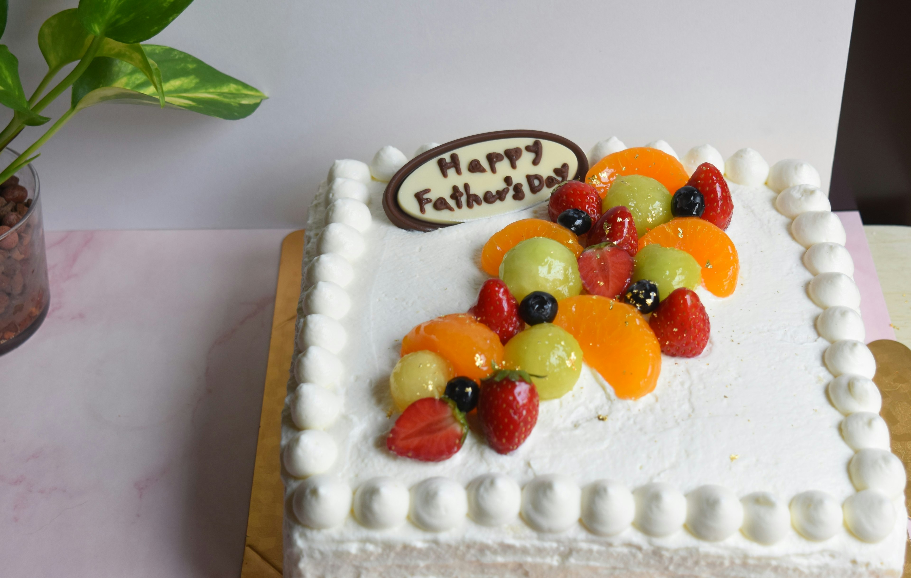 White cake decorated with fruit and a chocolate plaque saying Happy Father's Day