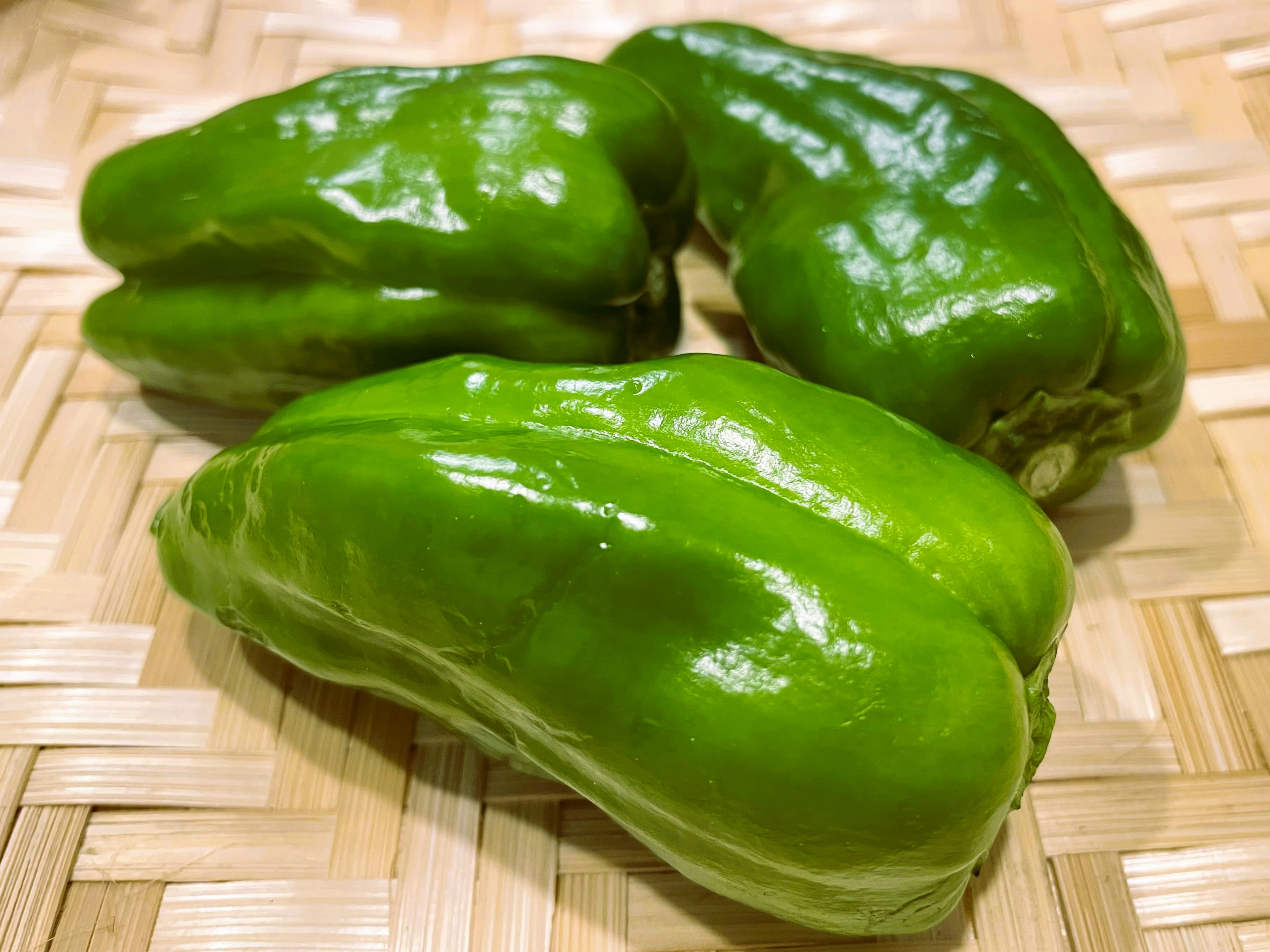 Trois légumes verts disposés sur une surface en bambou tressé