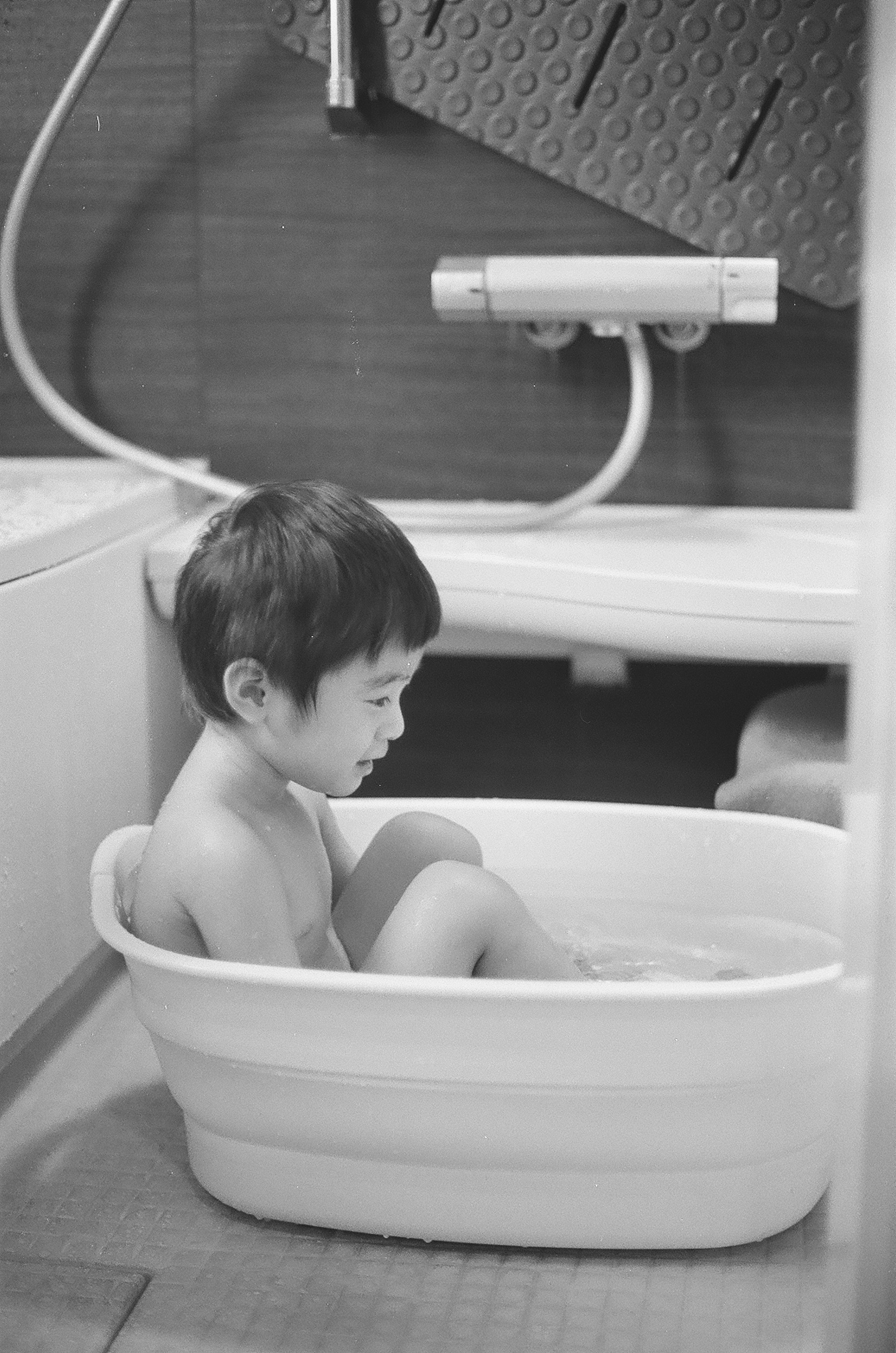 A small child sitting in a white bathtub in a black and white photo