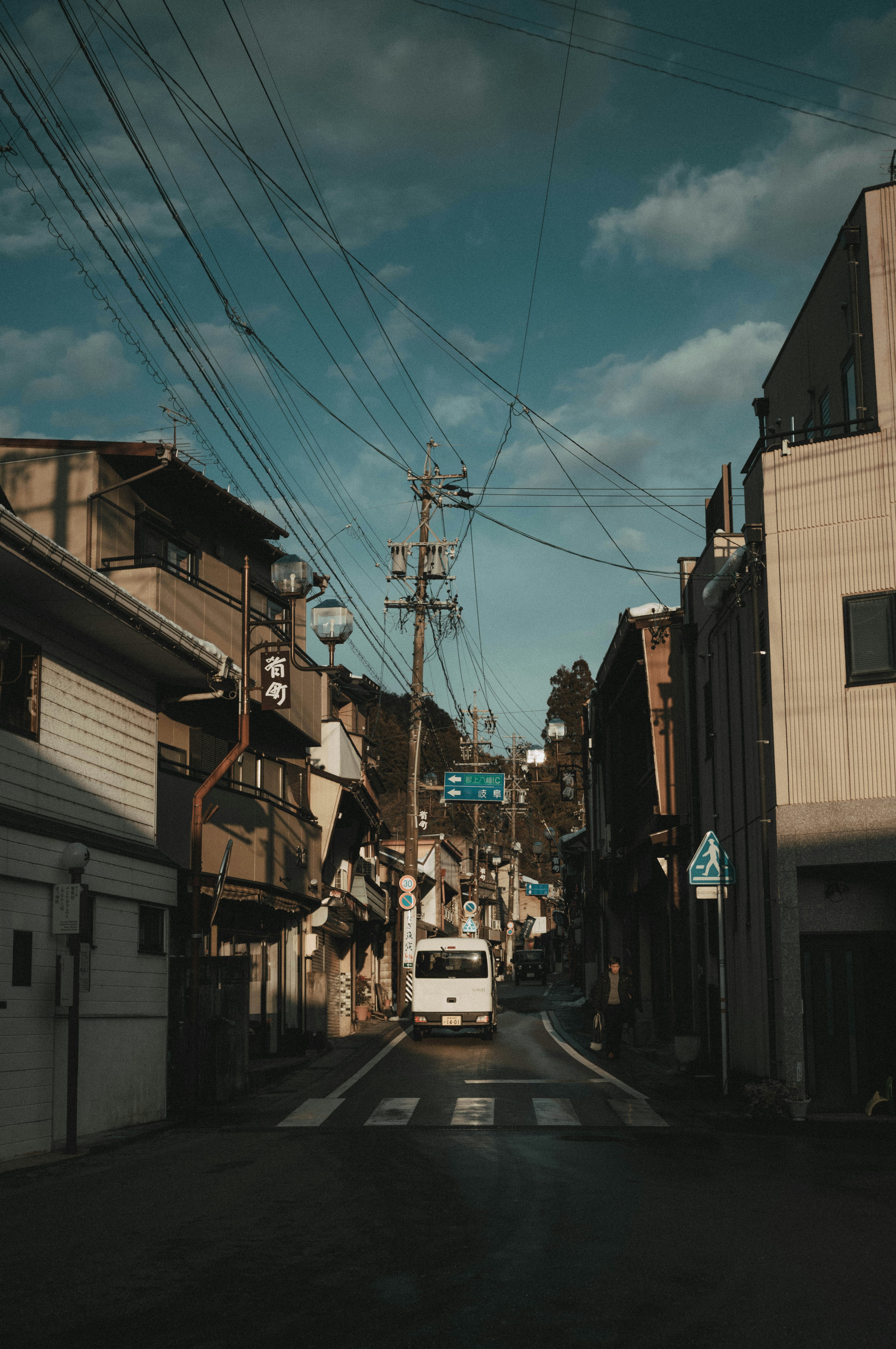 狭い道を走る白いトラックと周囲の建物が映る風景