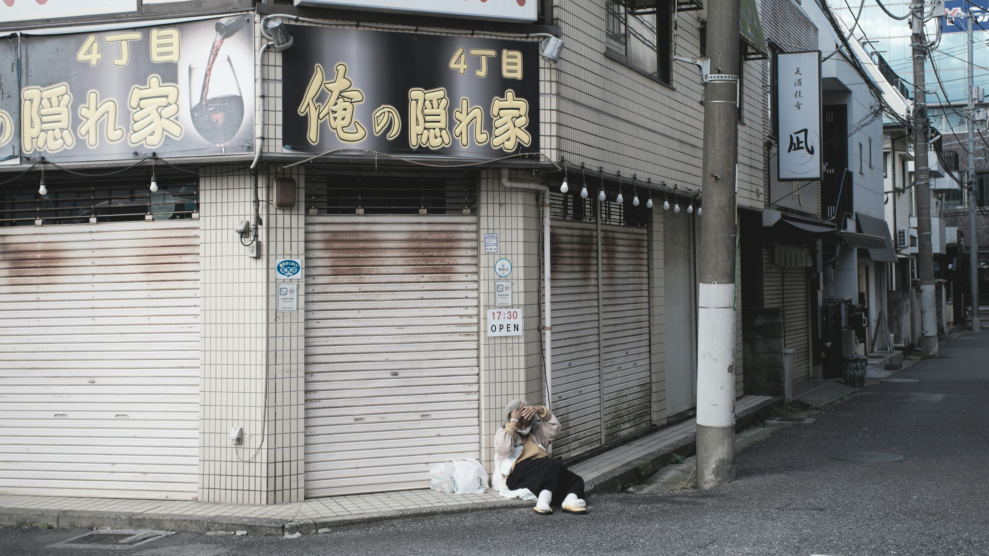 閉まった店舗の前に座る人物と周囲の街並み