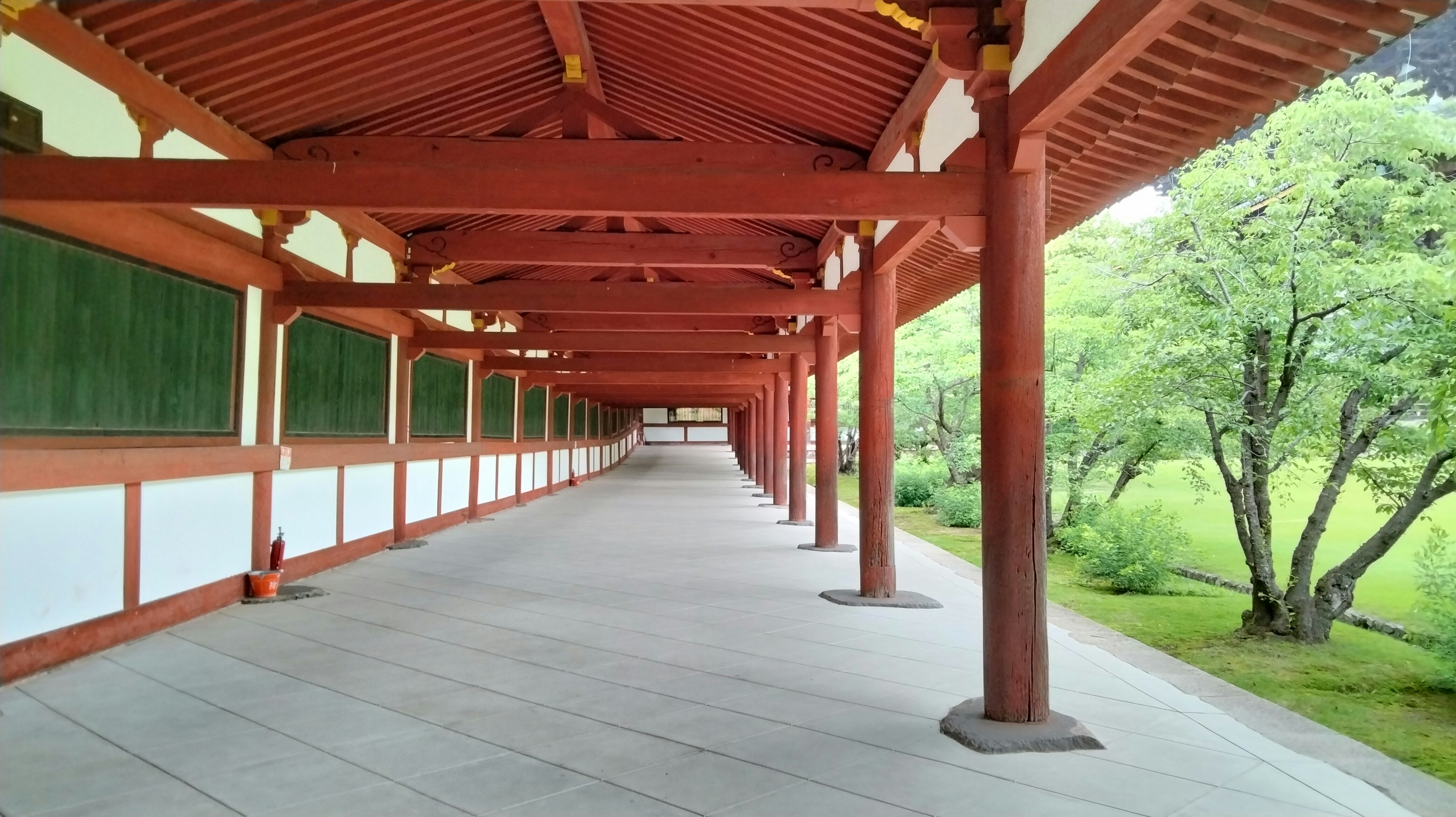 A corridor with beautiful red pillars and white walls leading to a green garden