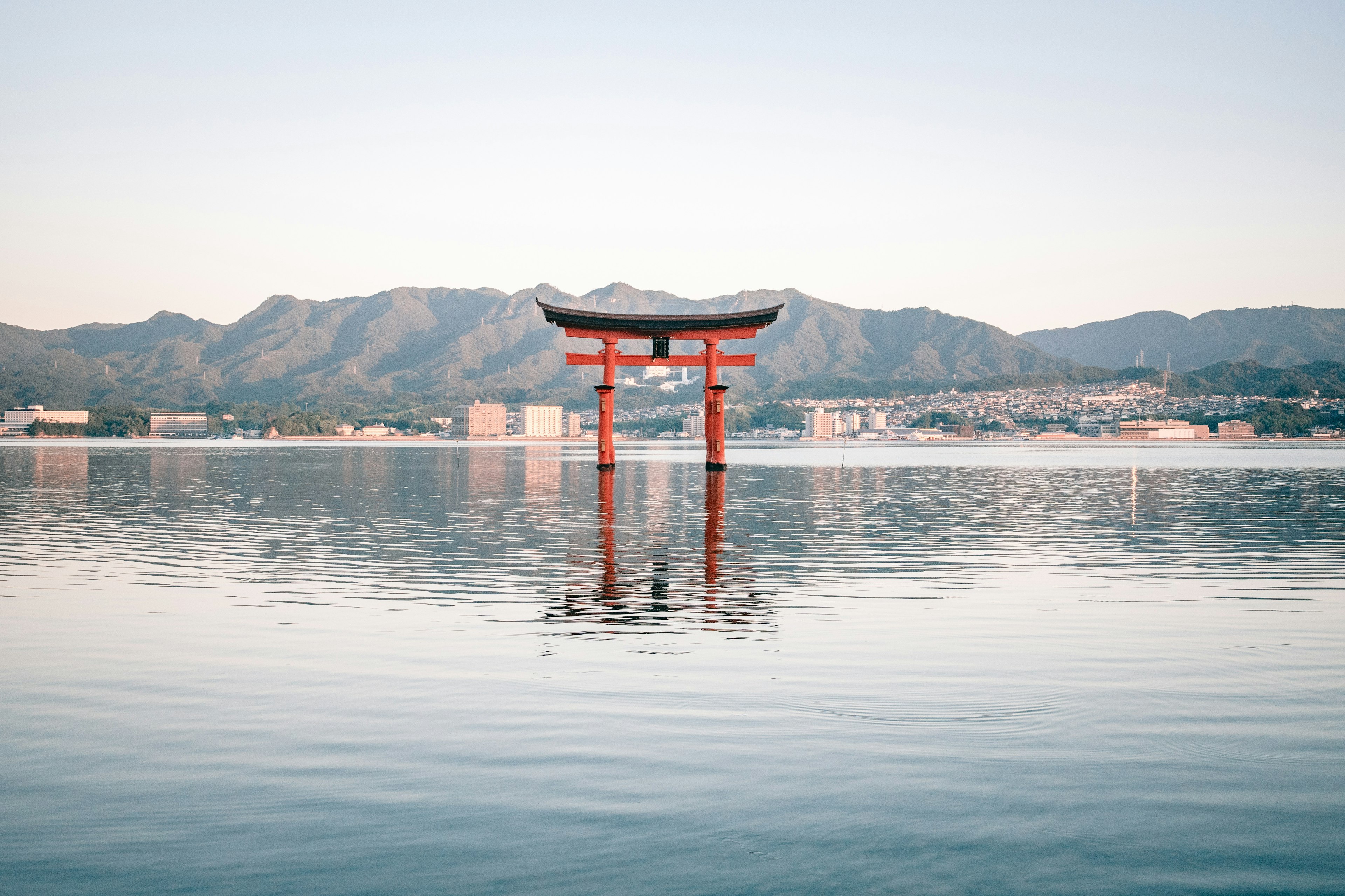 Gerbang torii merah yang dipantulkan di air dengan pegunungan di latar belakang