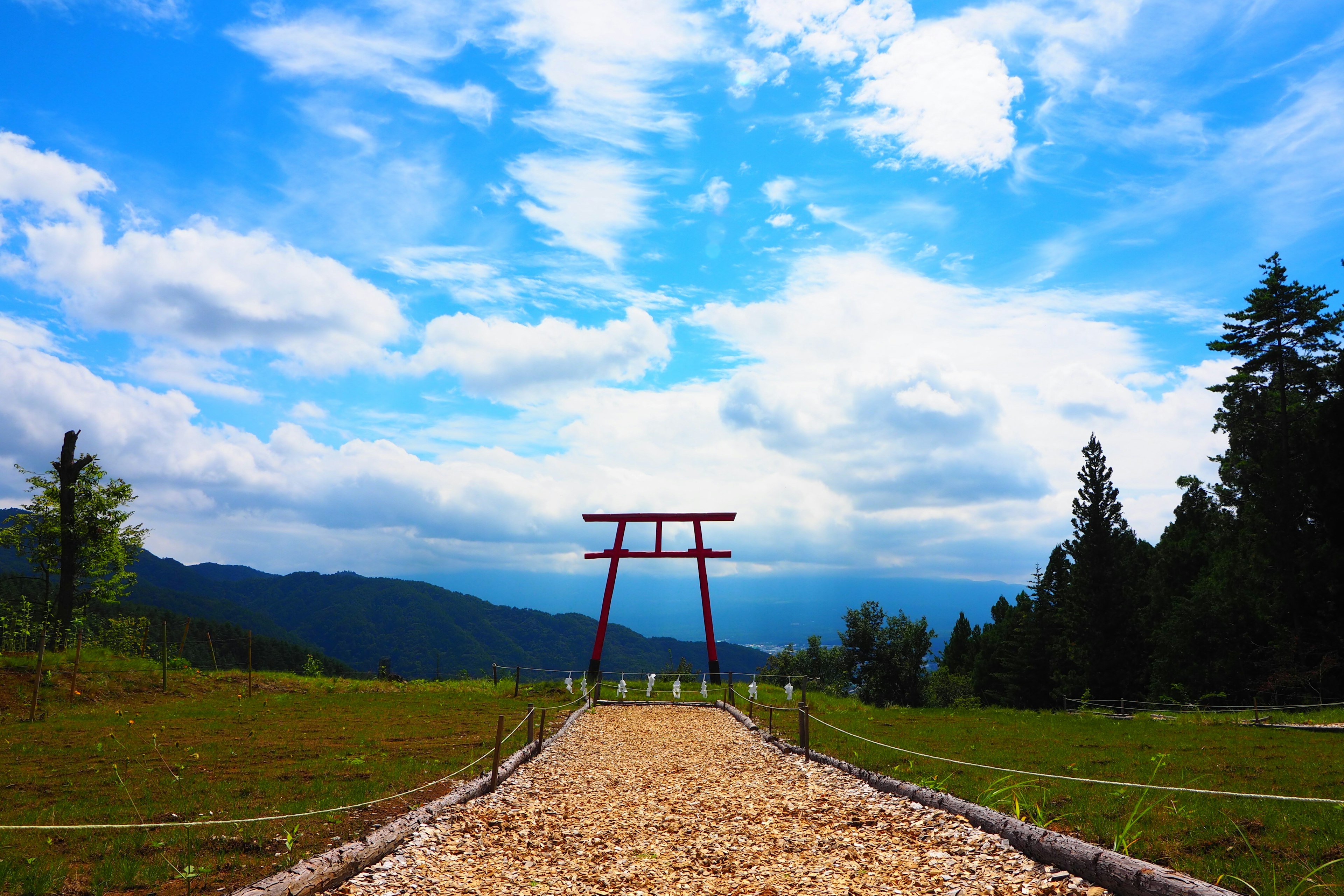 Chemin menant à un torii rouge avec des montagnes et un ciel bleu