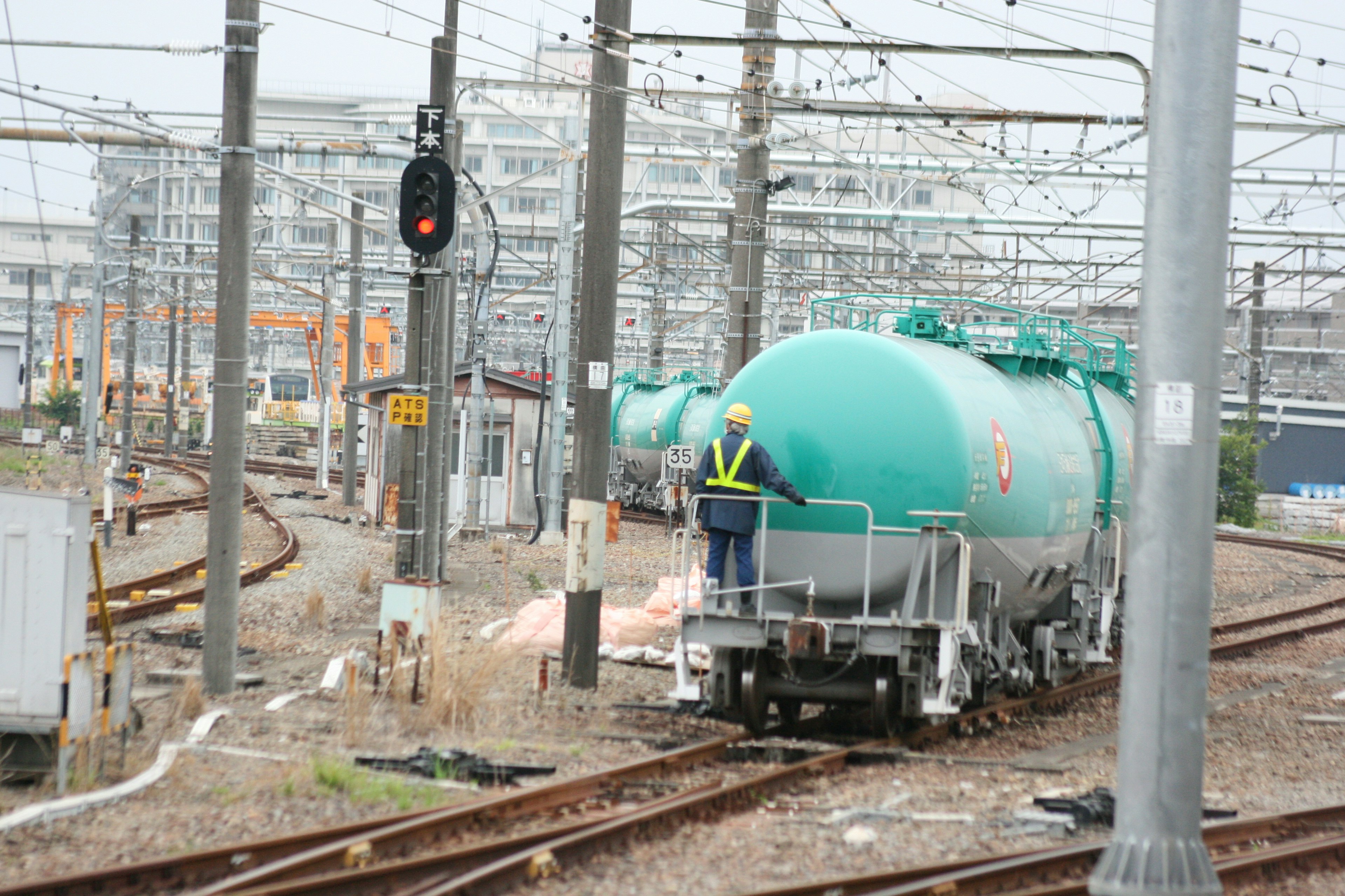 A green tank car is parked on the tracks with a worker standing on top Nearby signal and utility poles are visible