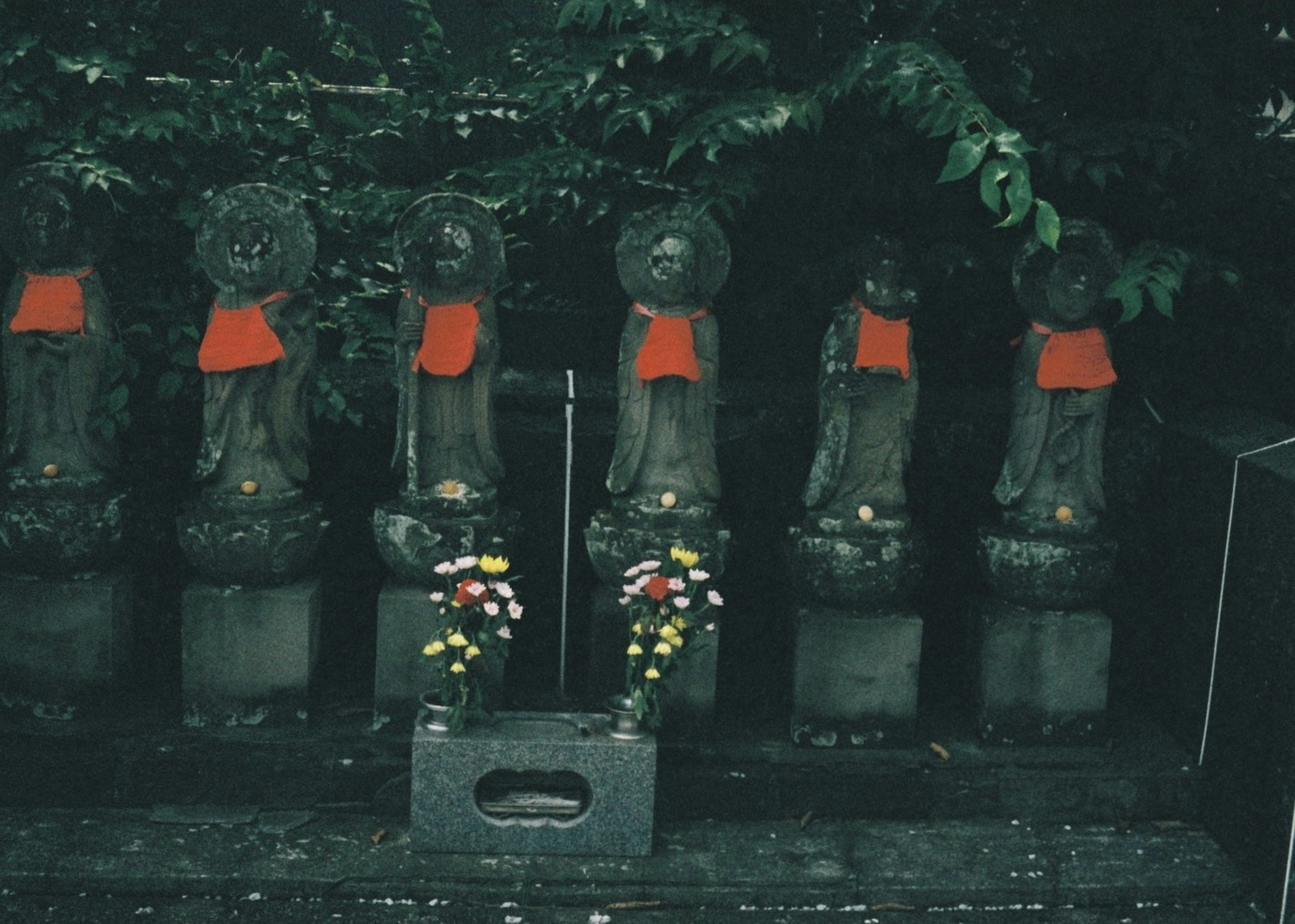 Fünf Statuen mit roten Lätzchen in einer ruhigen Umgebung umgeben von Grün