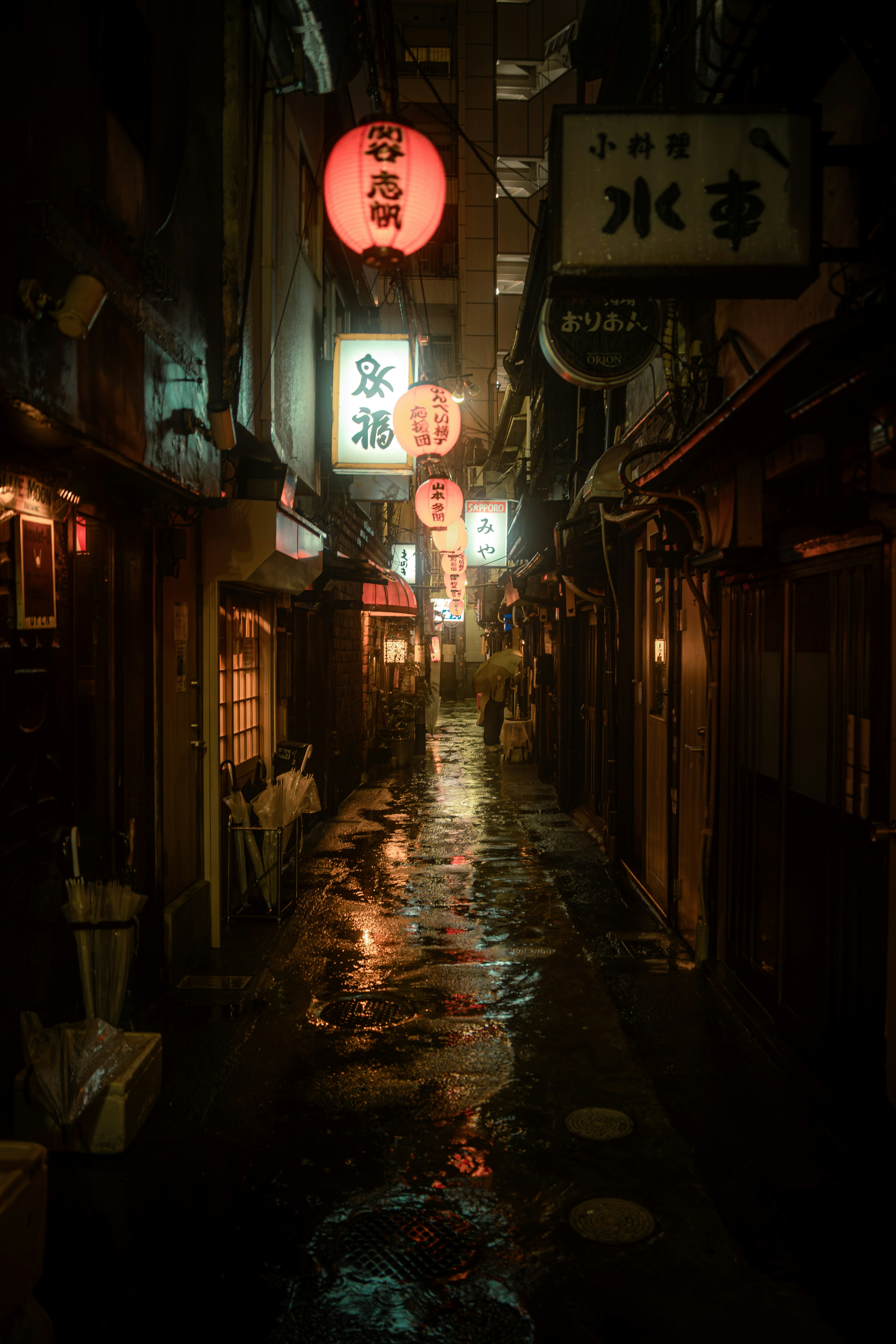 Narrow alley illuminated by colorful lanterns reflecting on wet pavement