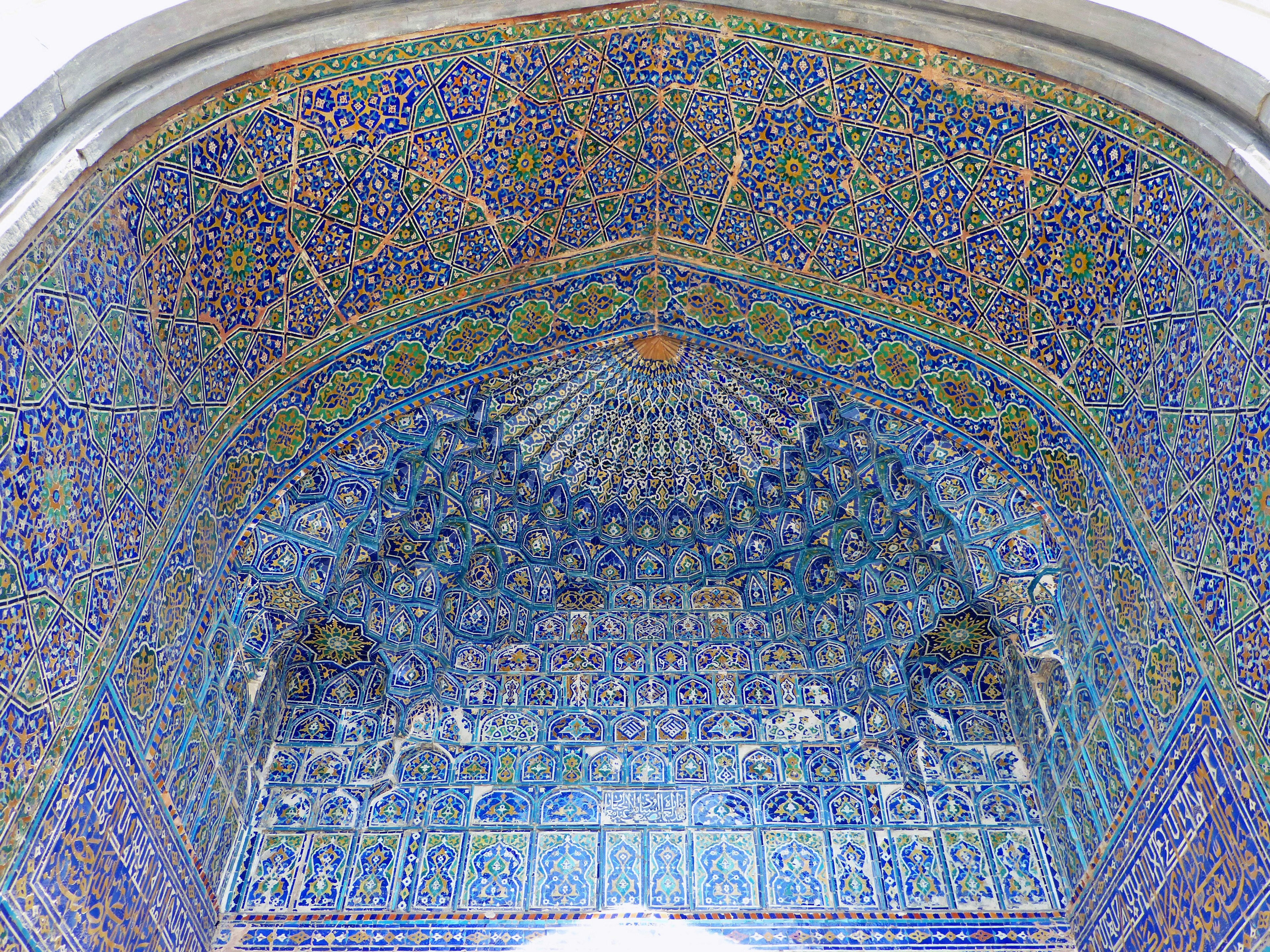 Intricate blue tile work and colorful patterns on an arched ceiling in Islamic architecture