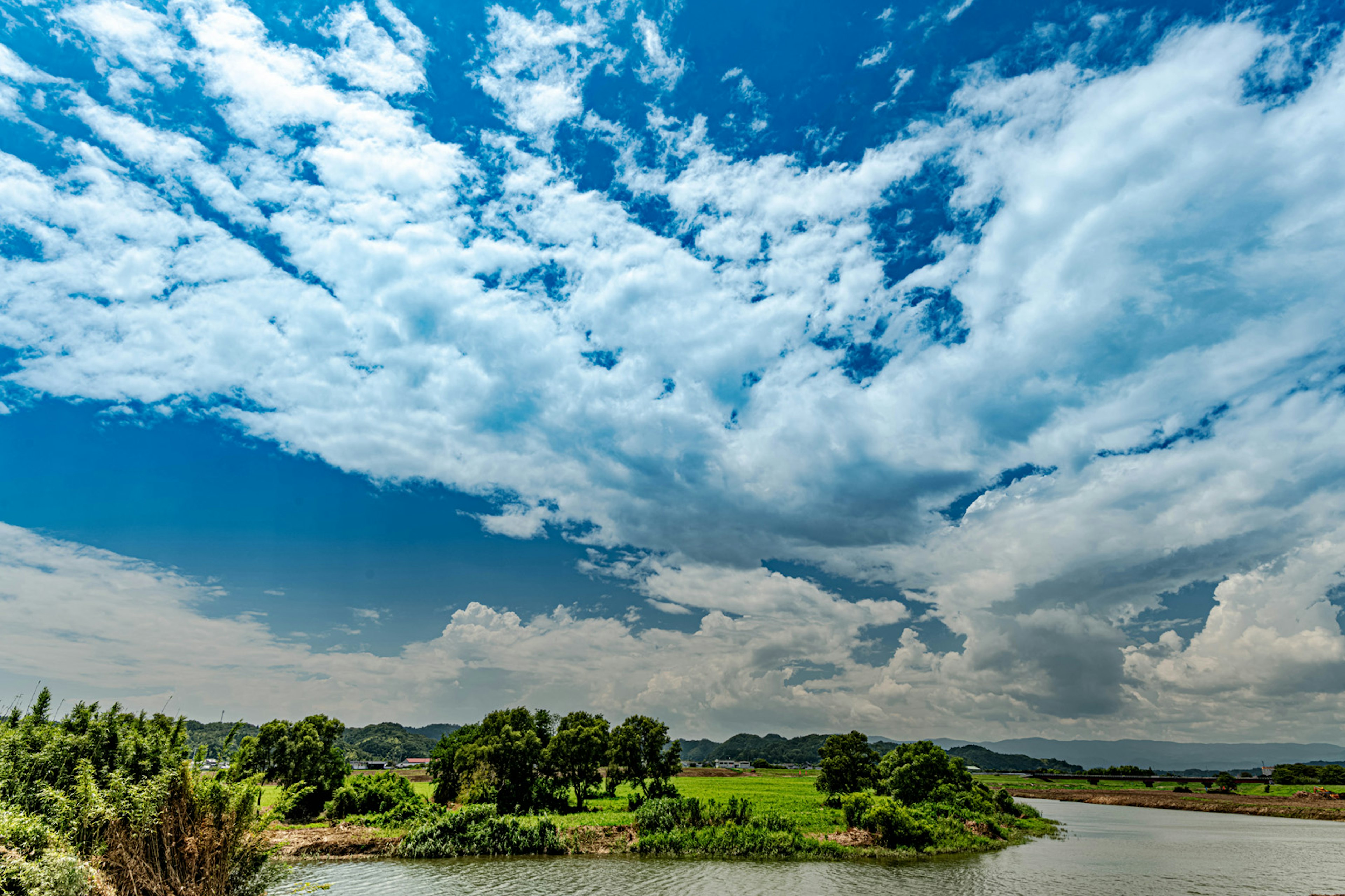 Vista panoramica di un cielo blu con nuvole bianche rive verdi e un fiume tranquillo