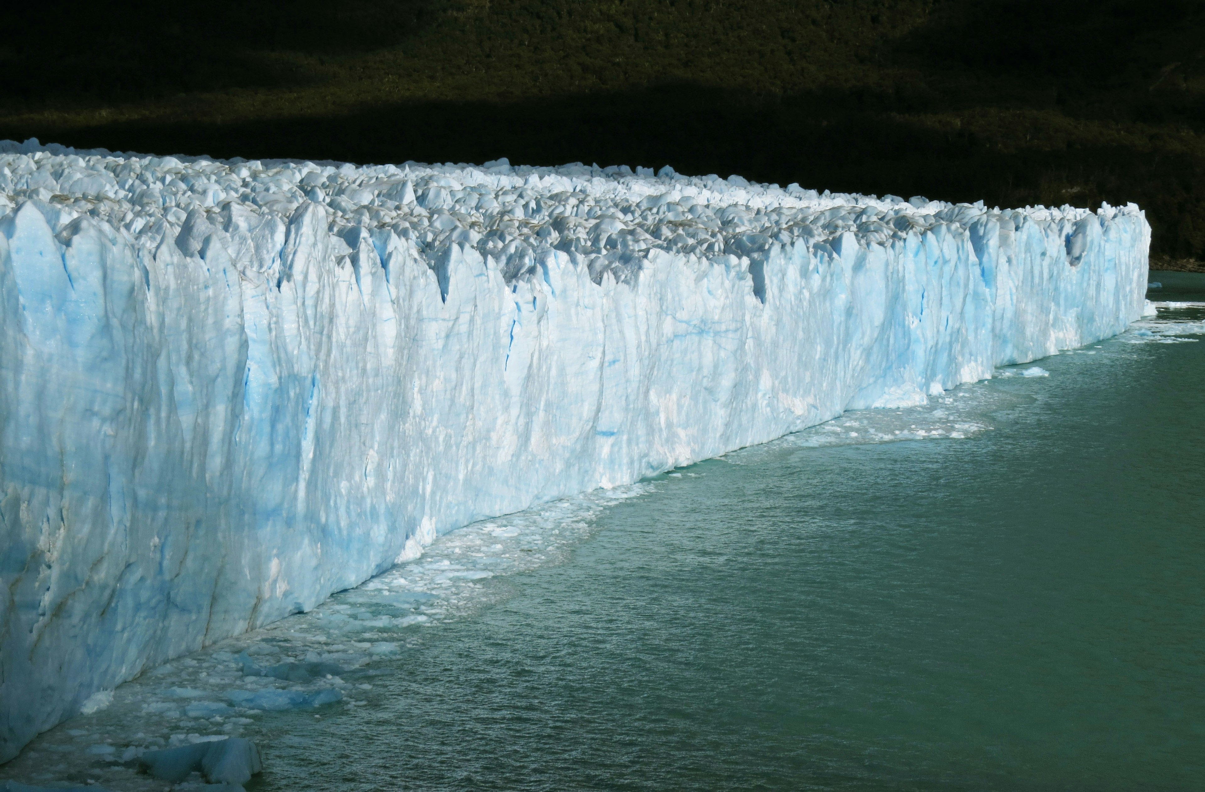 Glacier ice wall with shades of blue and water surface