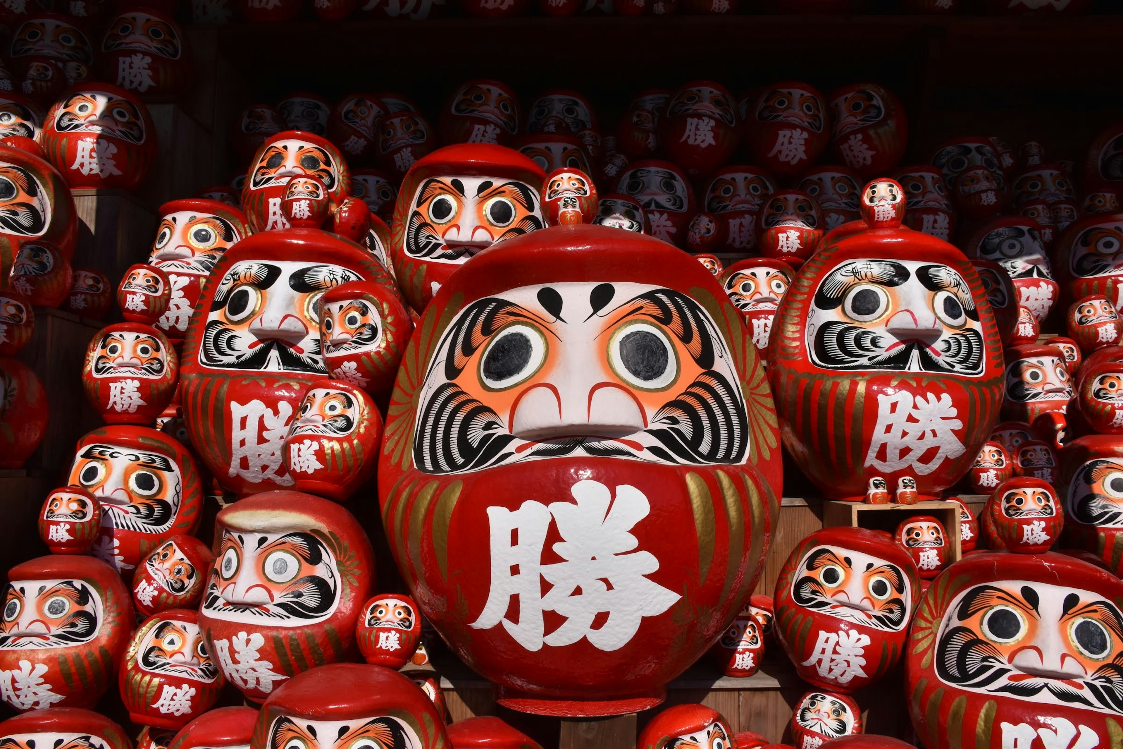 A collection of red Daruma dolls with a prominent character for victory