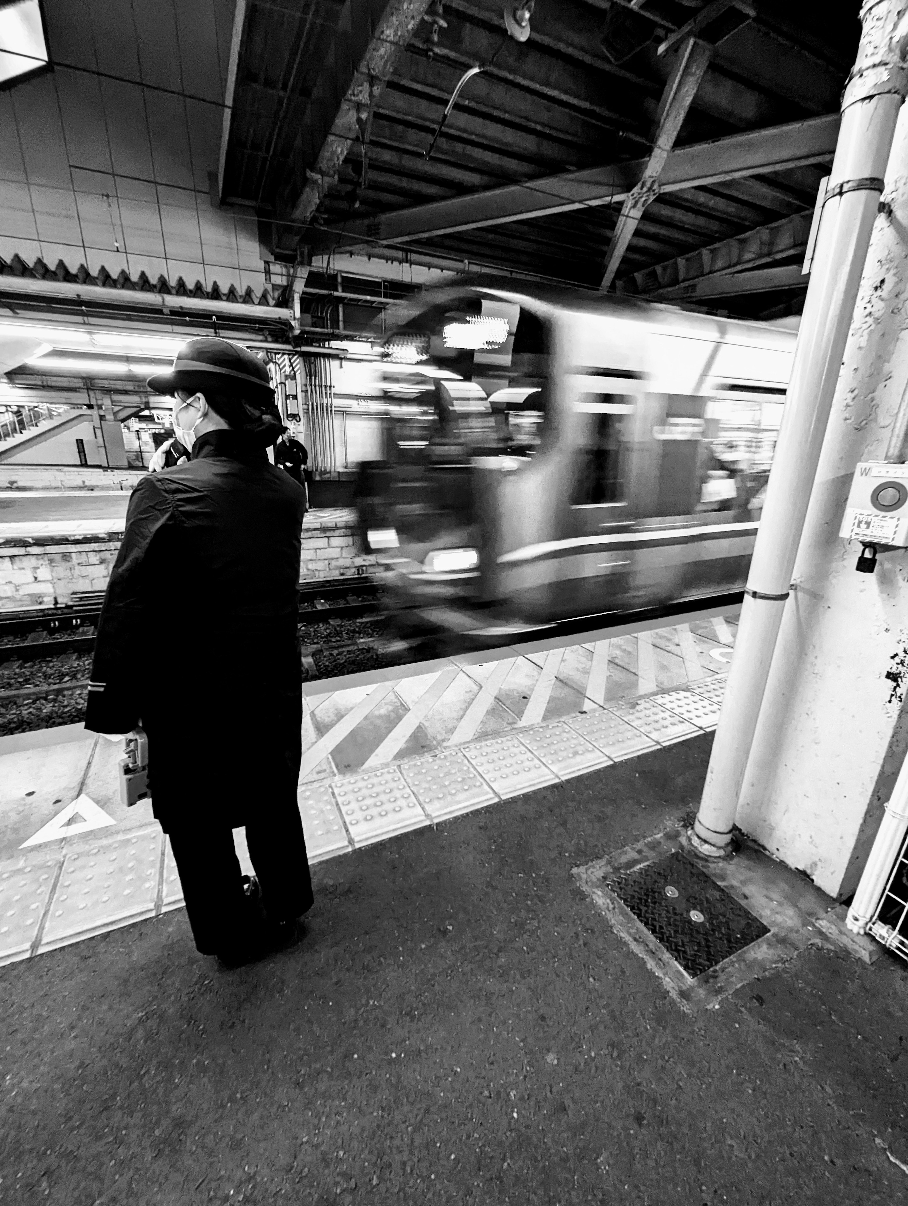 A silhouette of a person watching a train pass by at a black and white station