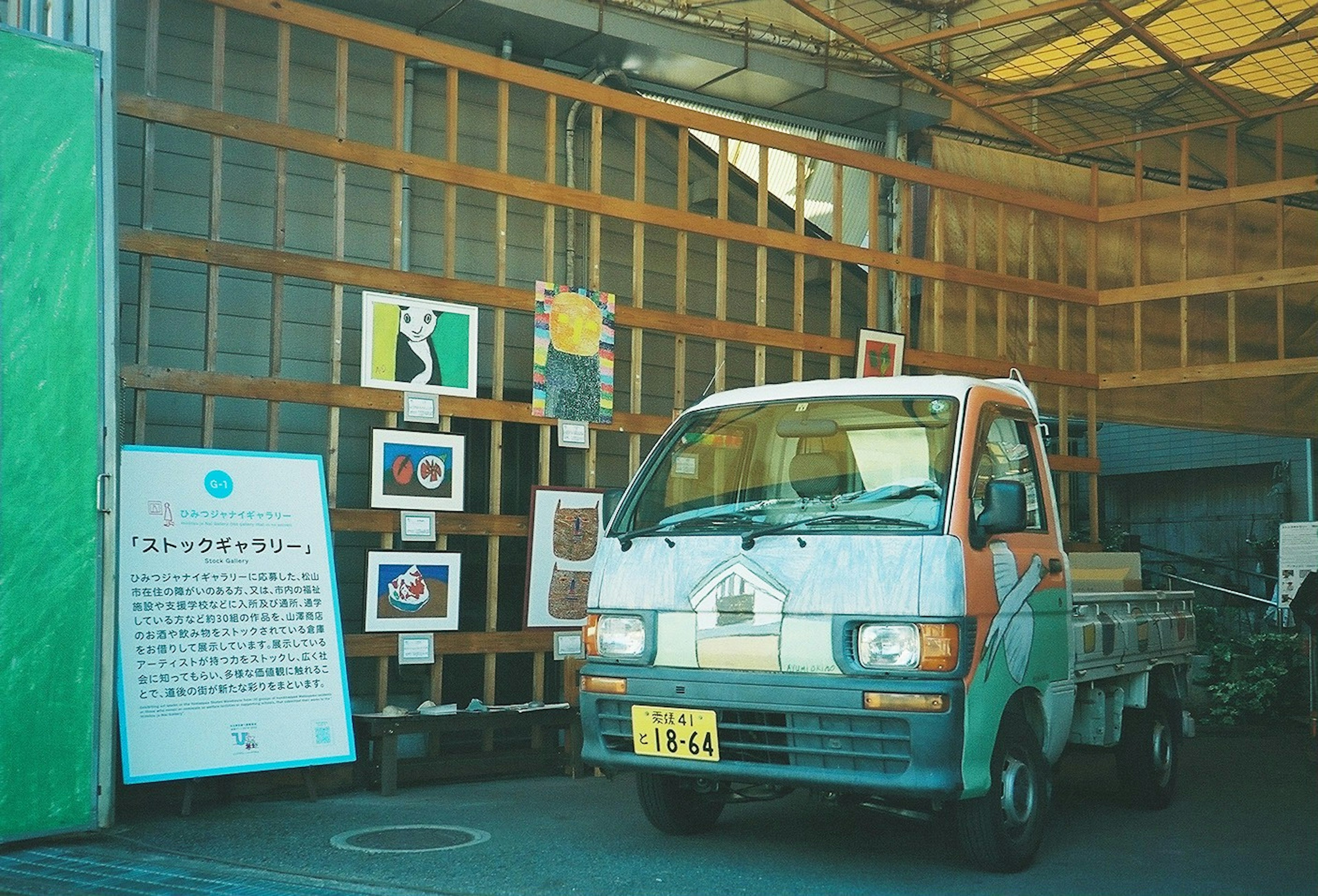 A small truck parked inside a warehouse with colorful art displayed on the walls