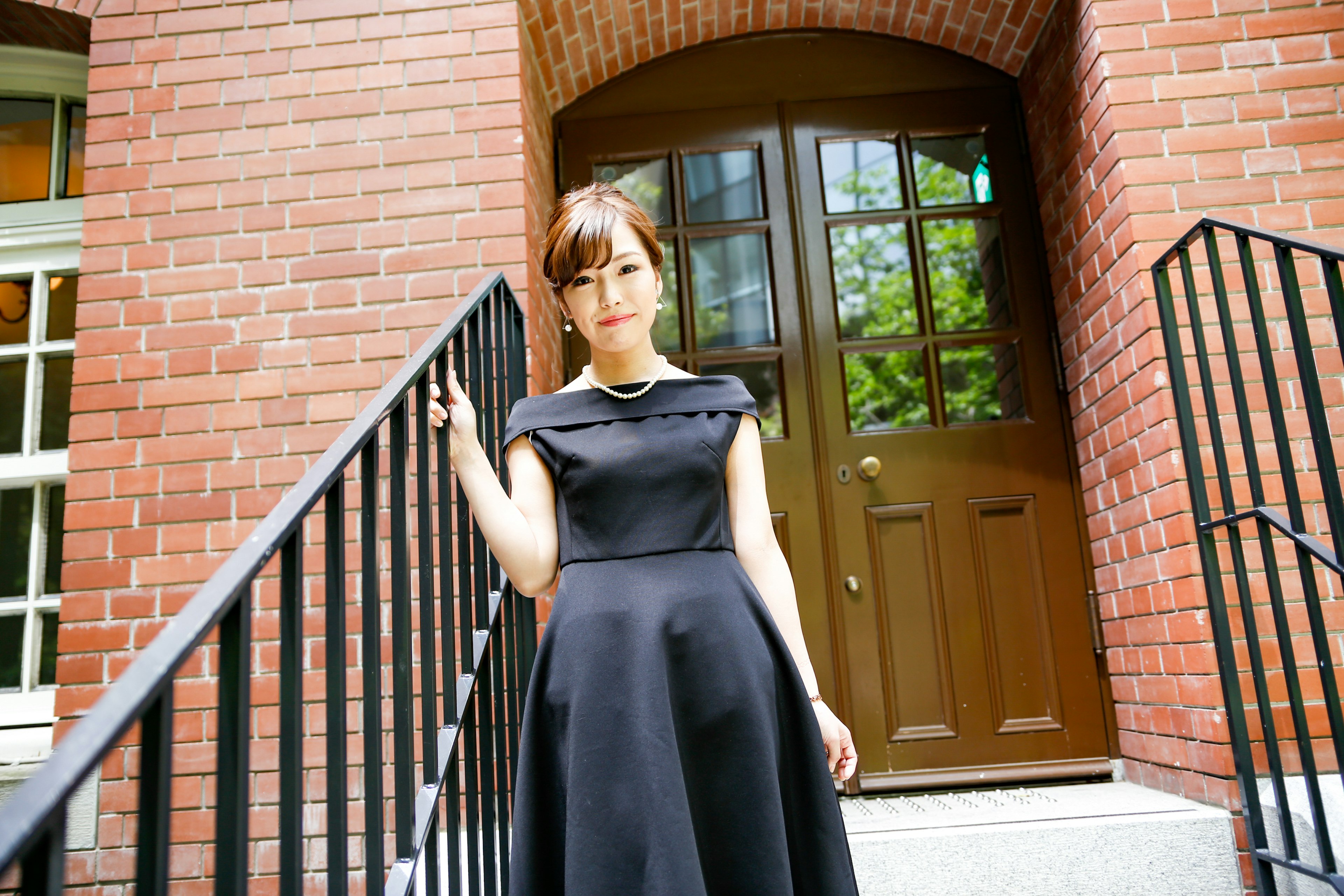 Woman in a black dress standing on stairs of a brick building