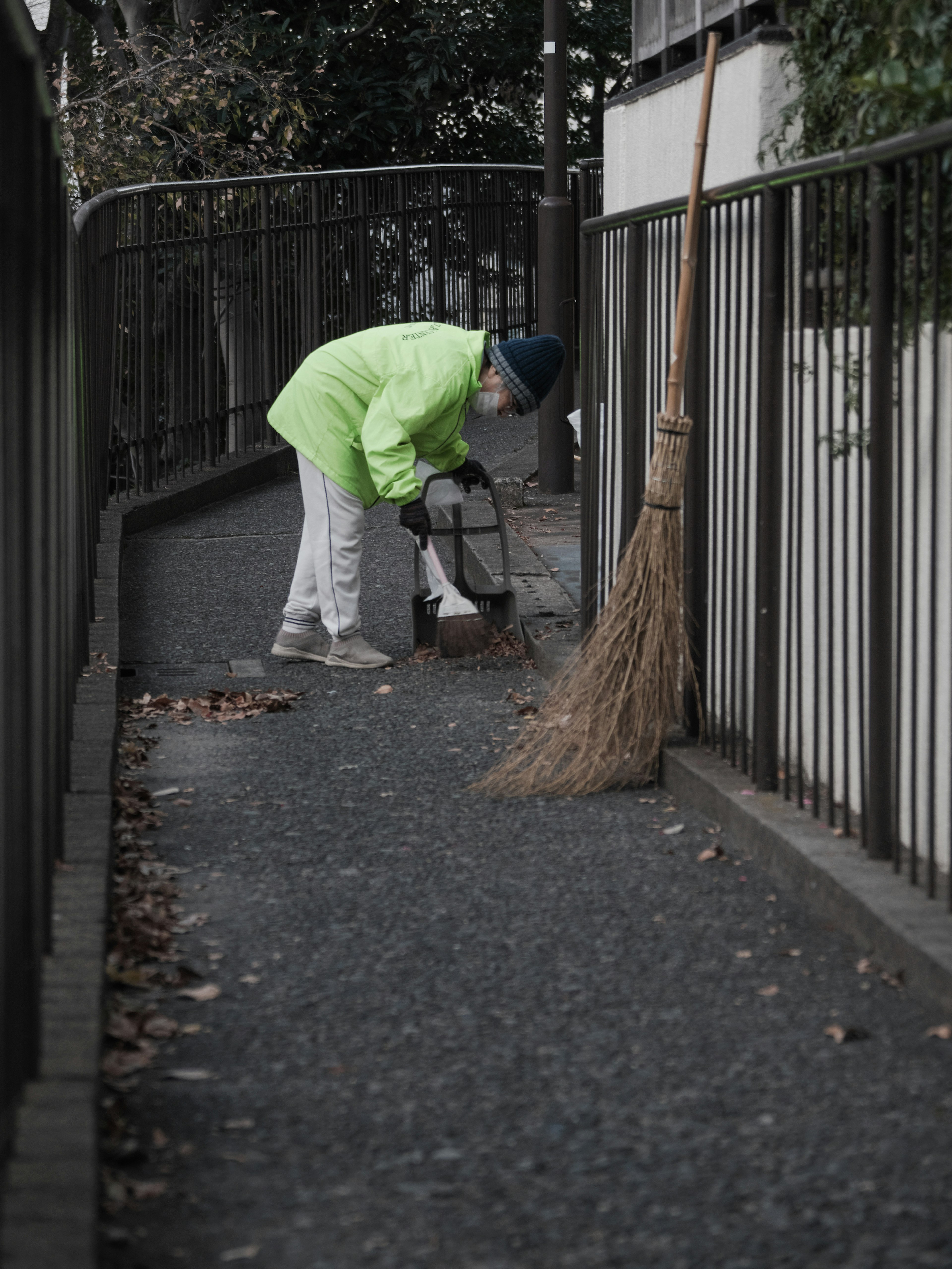 Personne âgée en manteau vert nettoyant un chemin