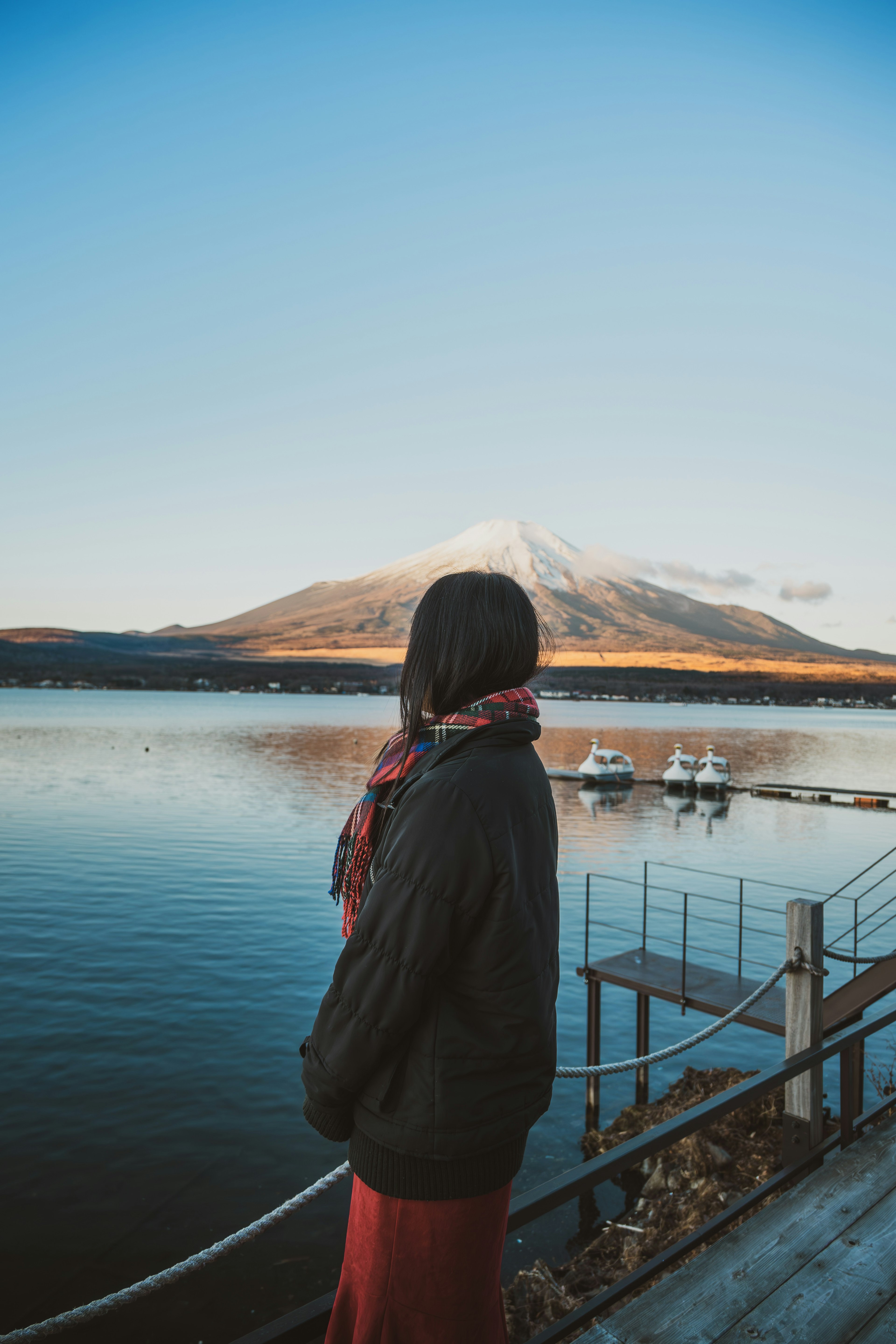 A woman standing by a serene lake with a snow-capped mountain in the background