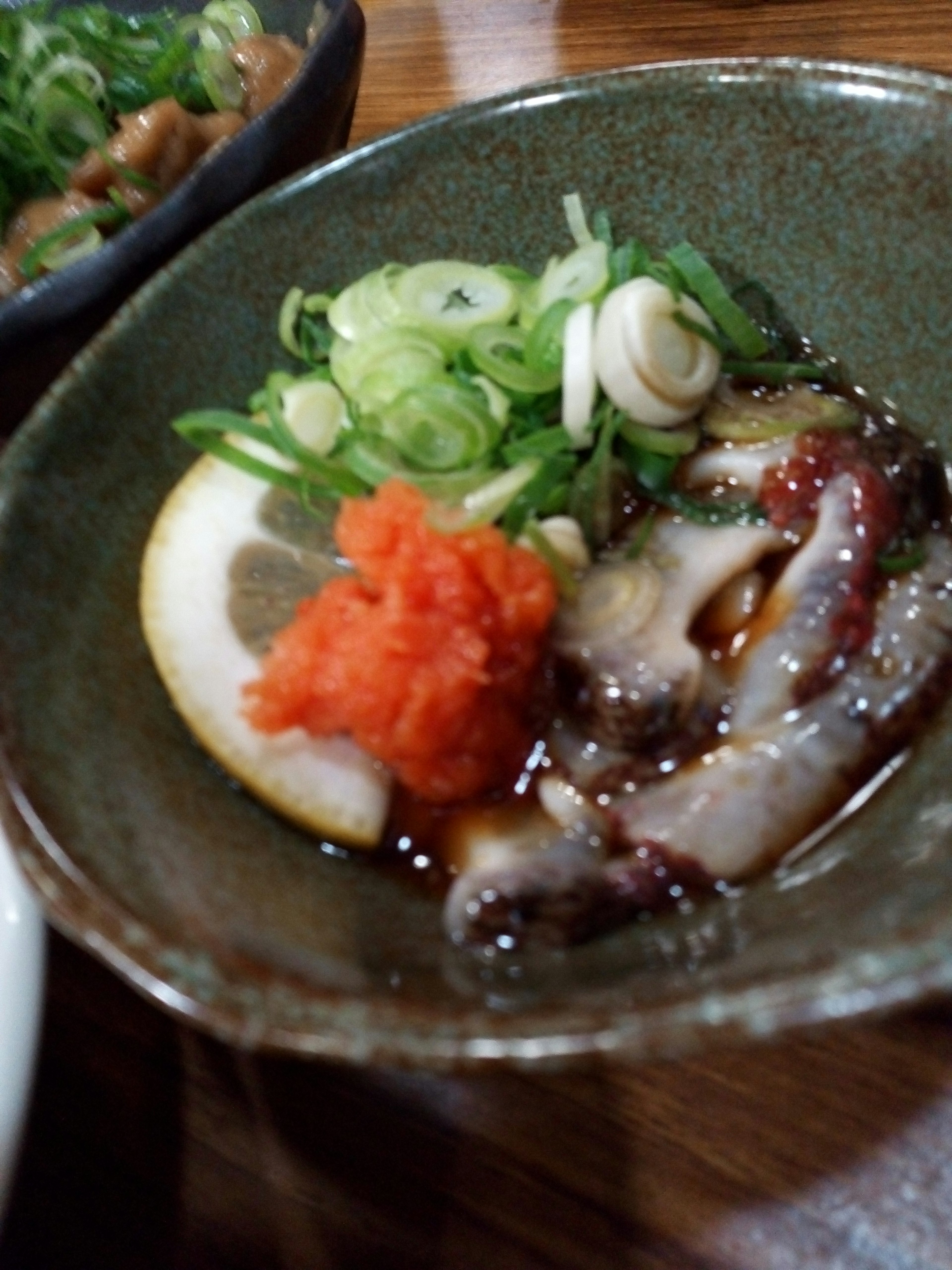 A small dish of Japanese appetizer featuring raw octopus garnished with green onions and yuzu with red chili paste