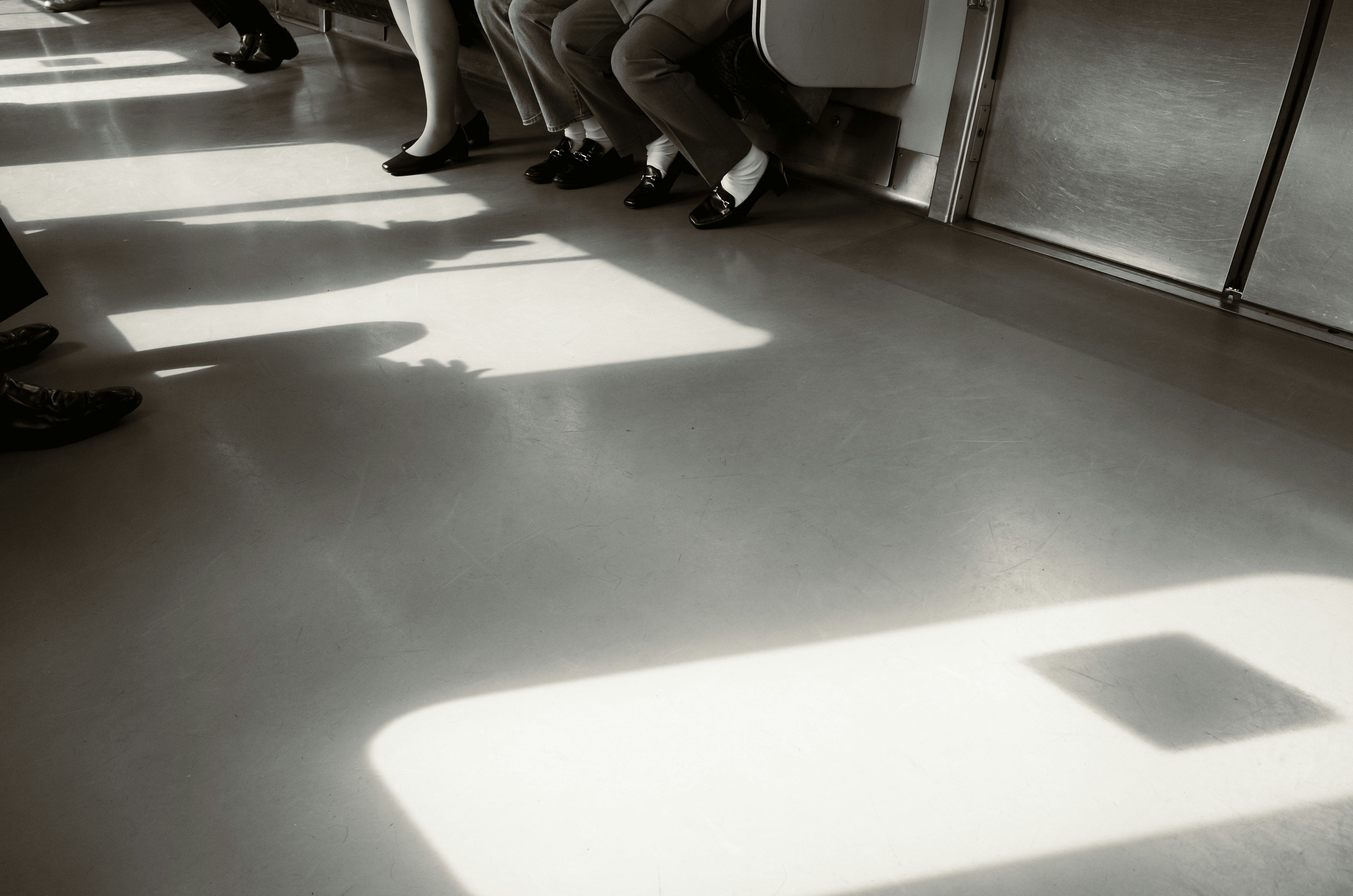 Foto von Füßen und Schatten von Menschen, die auf dem Boden eines Zuges sitzen