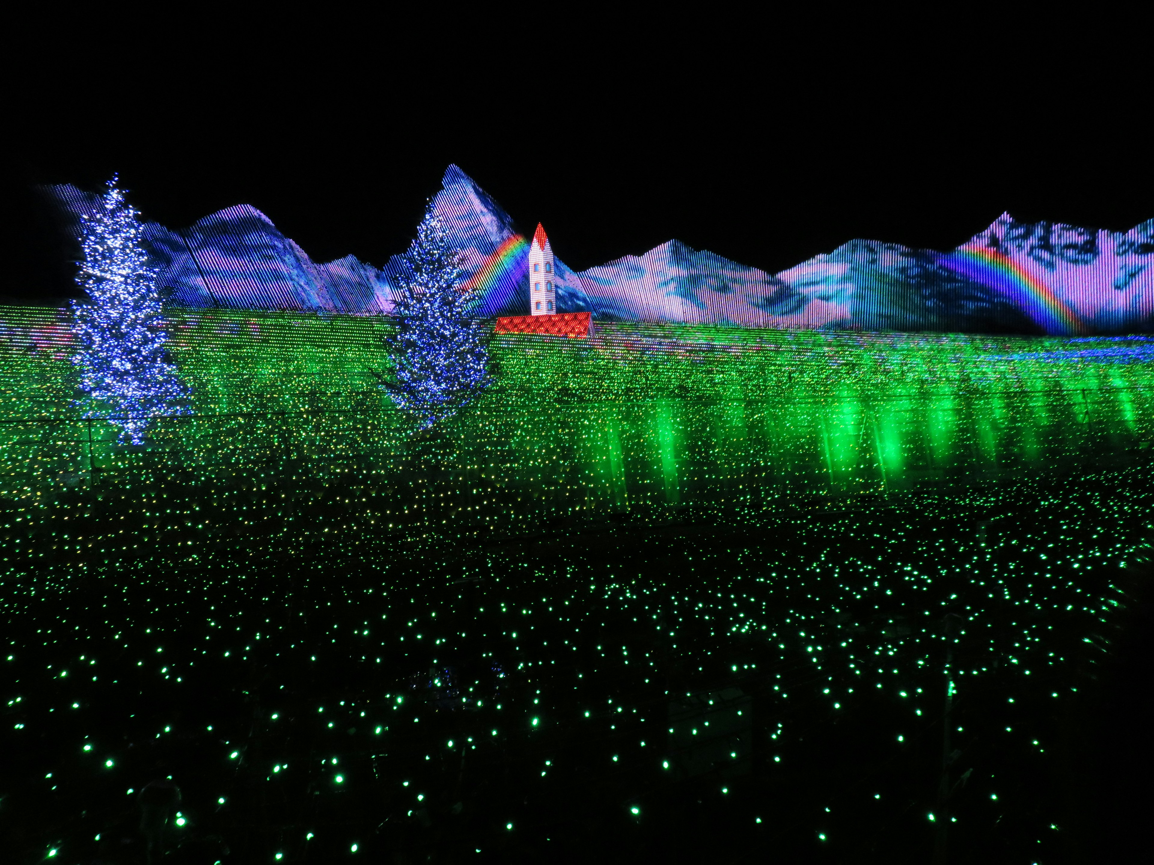 Vast green field illuminated with lights featuring a red tower and distant mountains