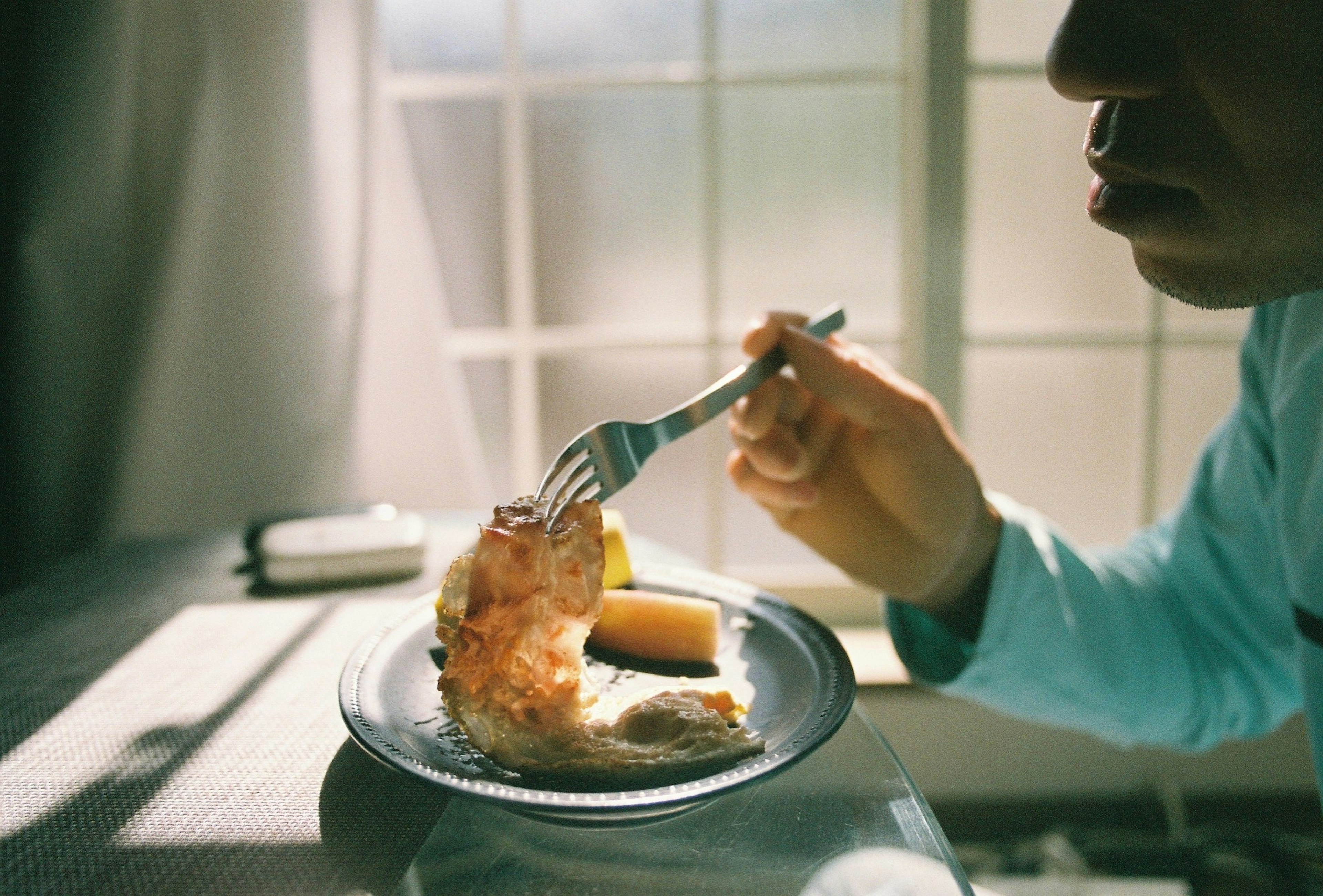 Die Hand eines Mannes, die eine Gabel mit Essen vor einem Fenster hält