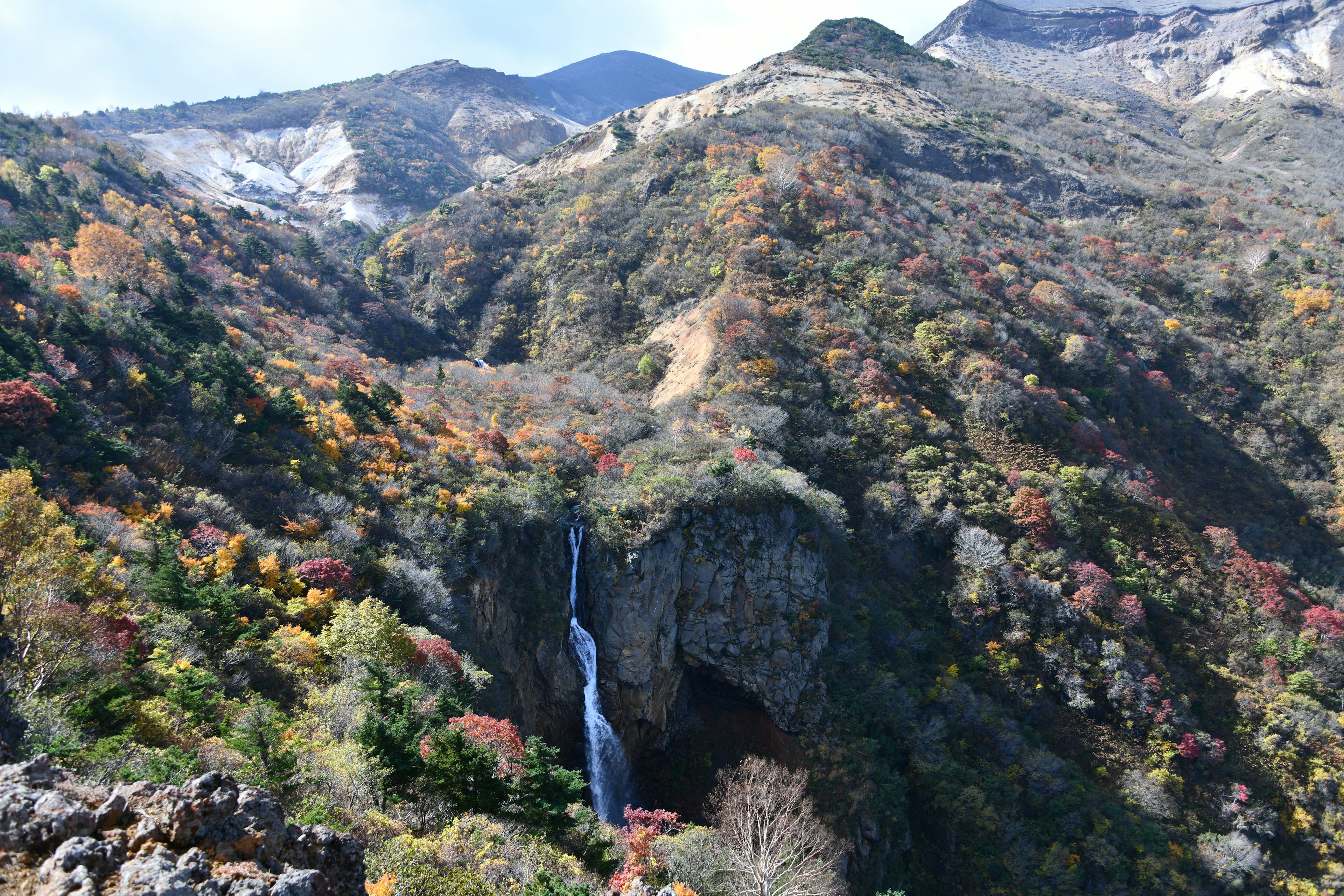 秋の紅葉に包まれた山々と滝の景色