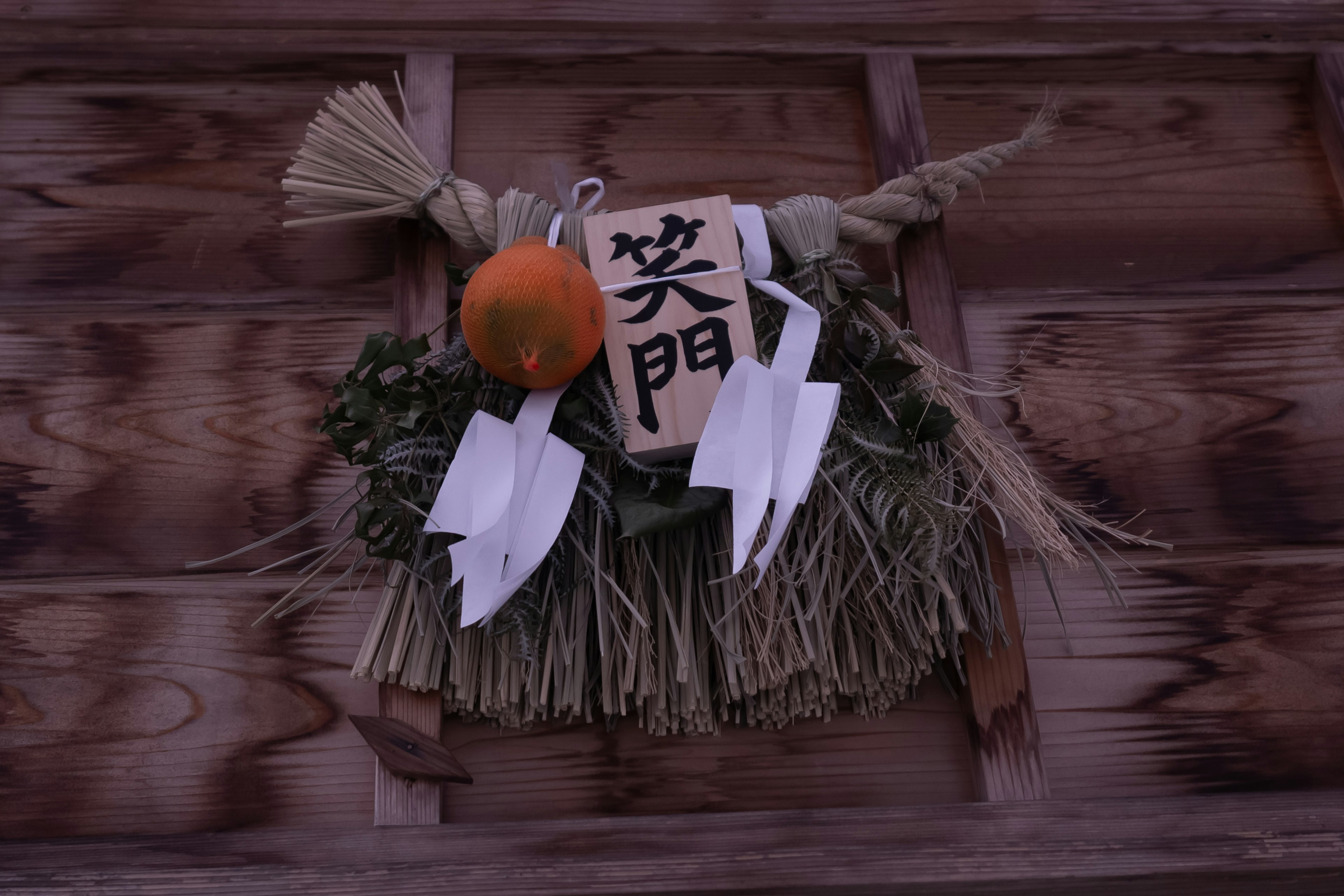 Décoration traditionnelle shimenawa avec une orange sur une porte en bois