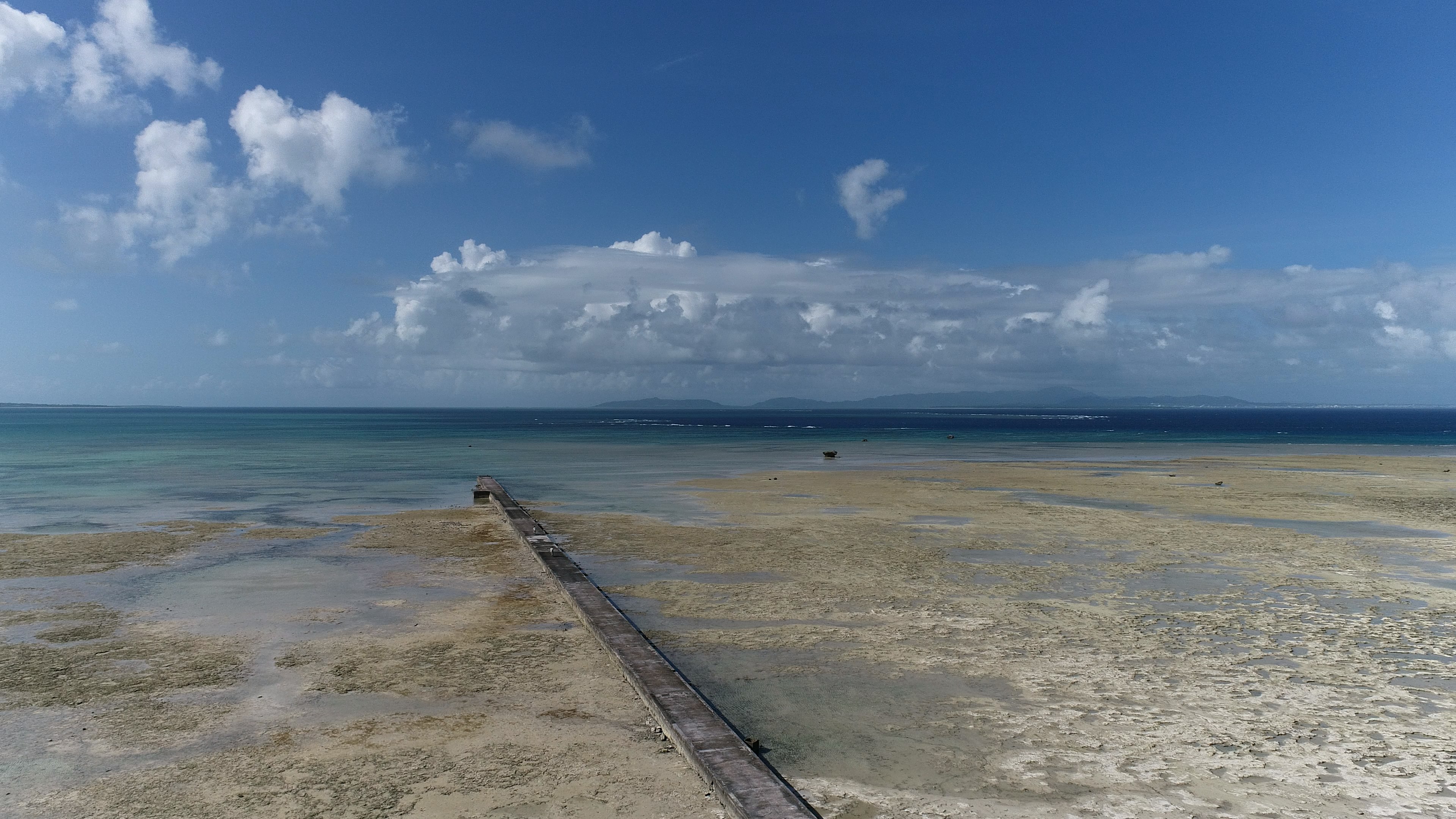 Scenic view of blue ocean and sky with a pier along the shore