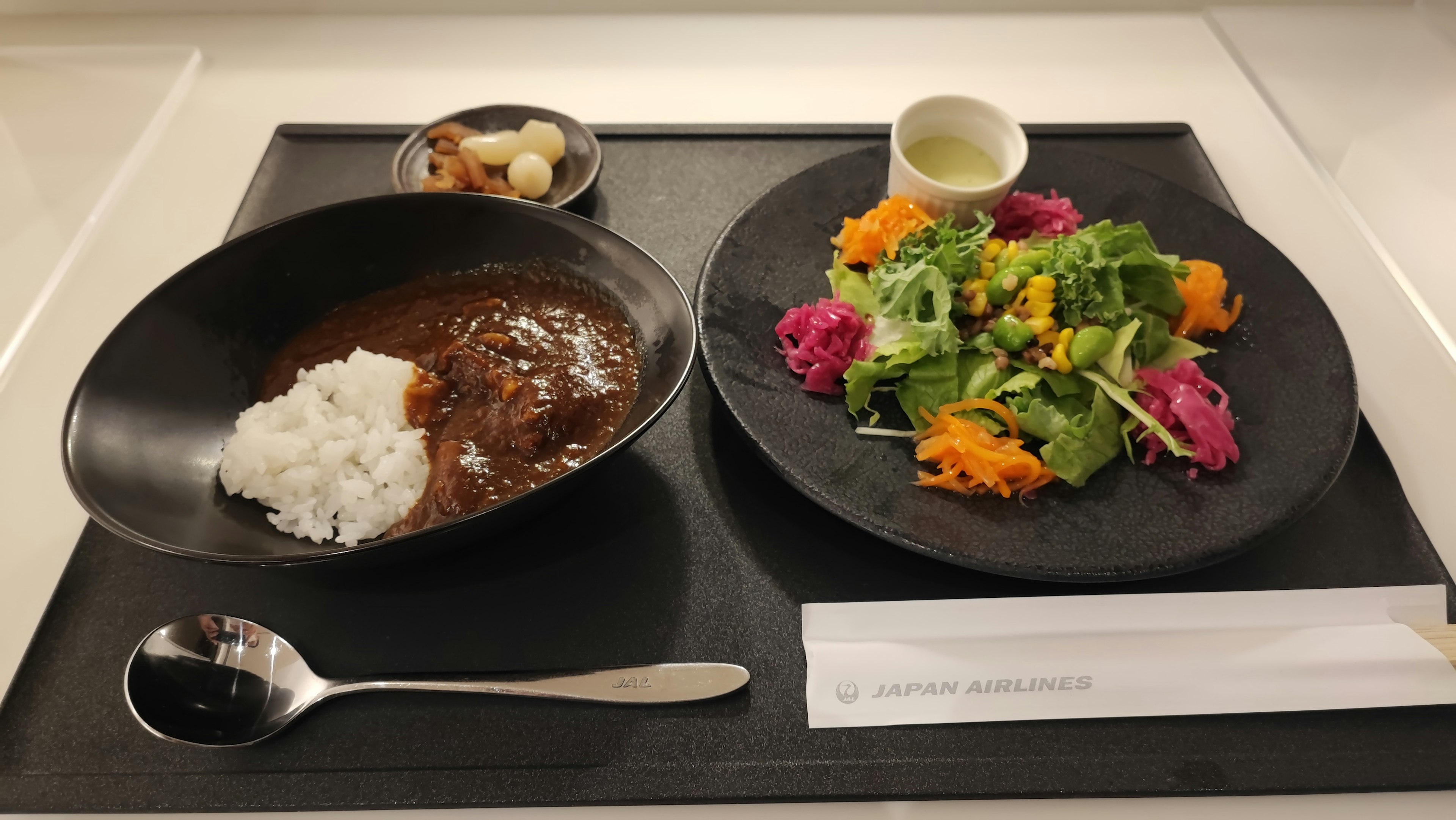 Riz au curry dans un bol noir avec une salade colorée sur une assiette noire