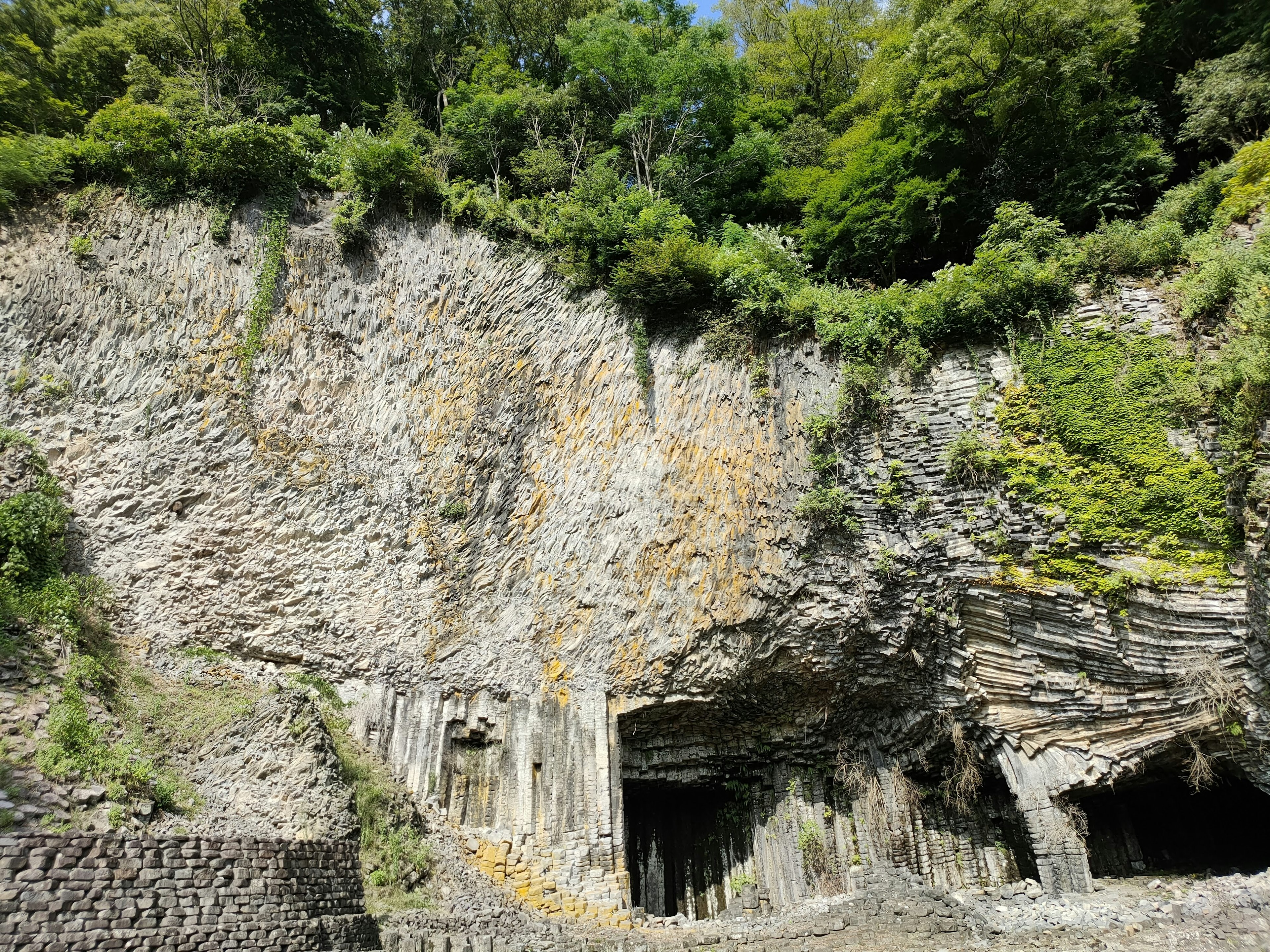 Large rock formation and cave entrance at the base of a green-covered cliff