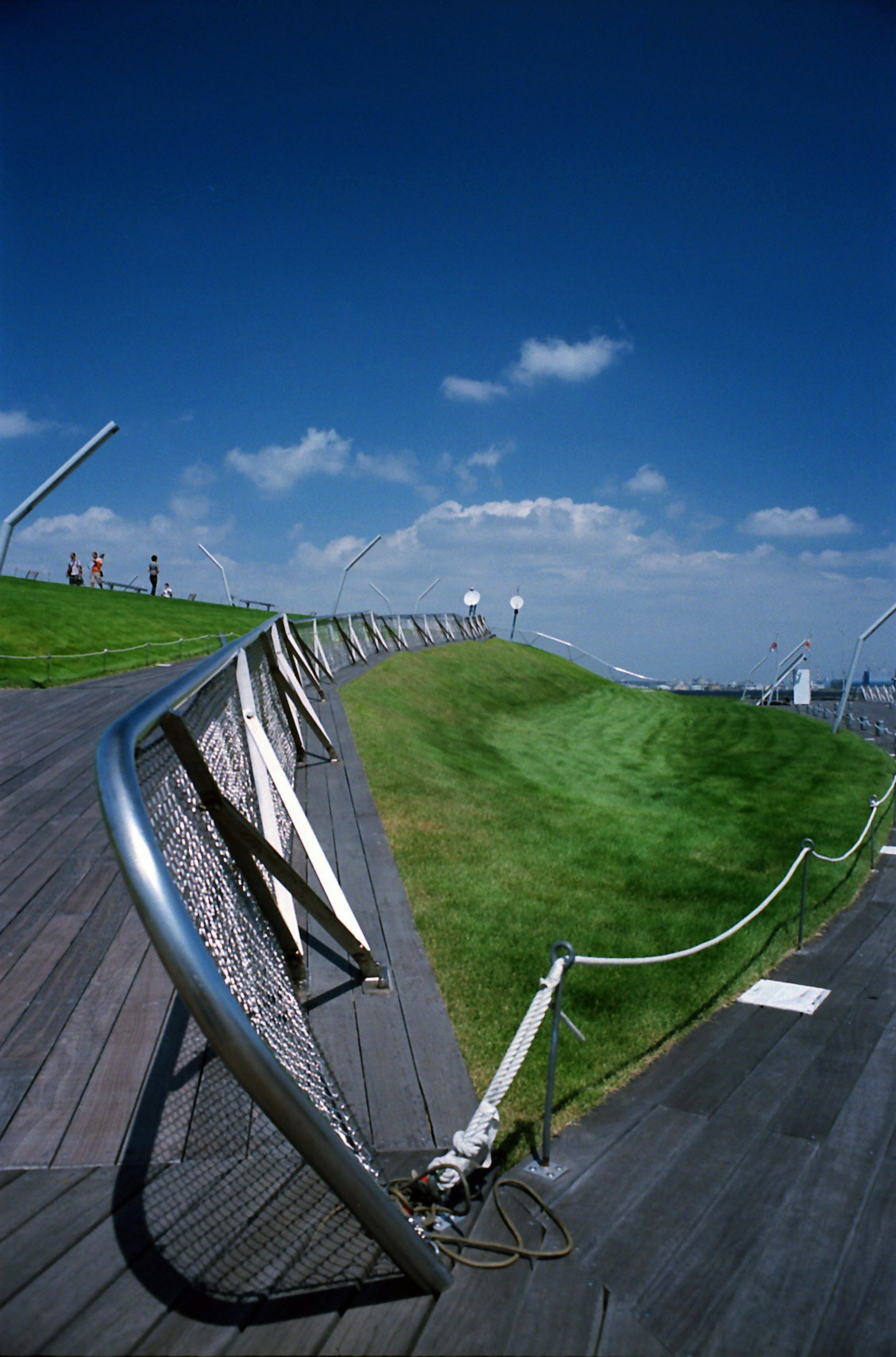 Landschaft mit einem grünen Hügel und einem Holzdeck unter einem blauen Himmel