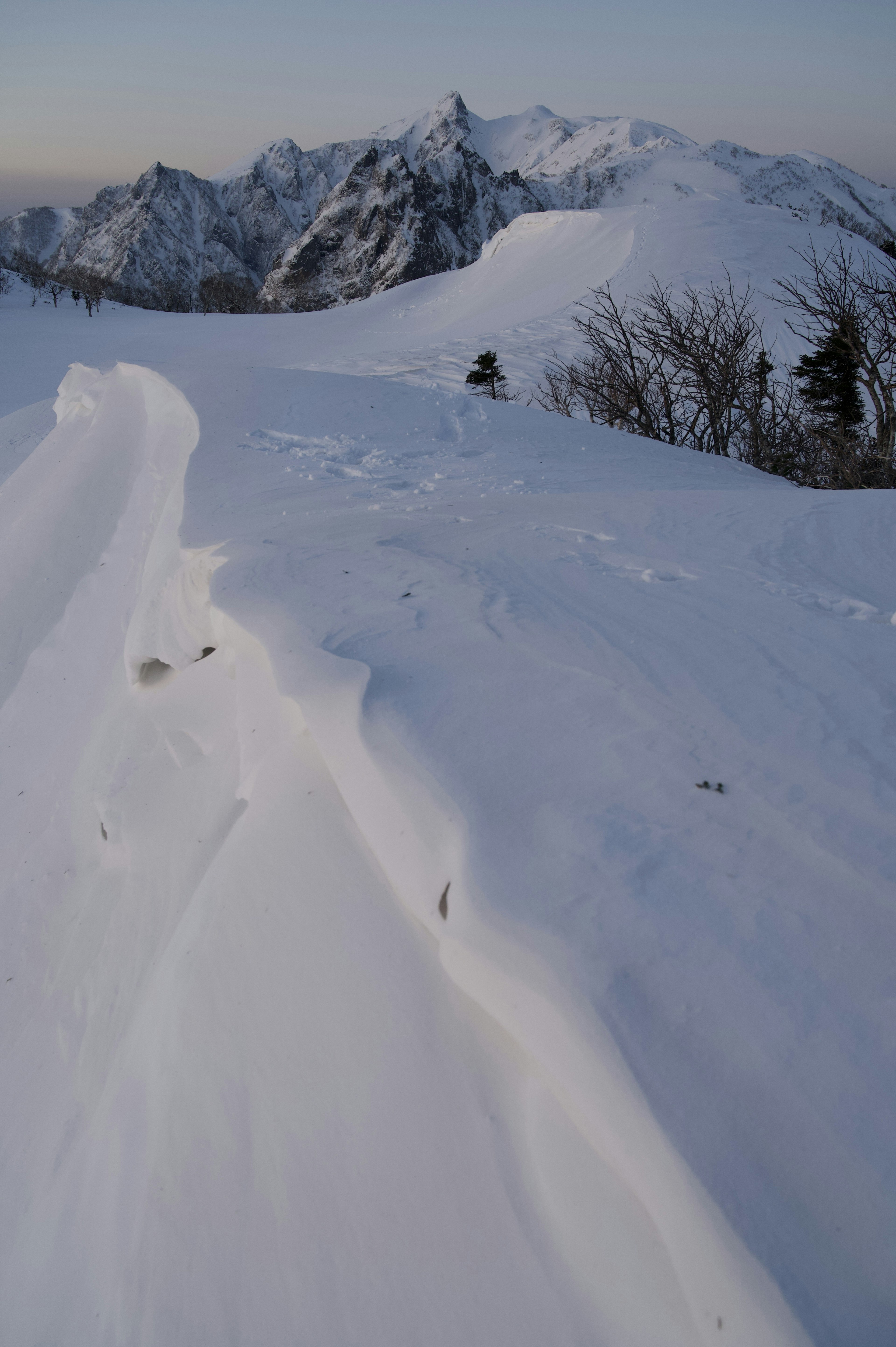 Paesaggio montano innevato con curve di neve lisce e picchi lontani