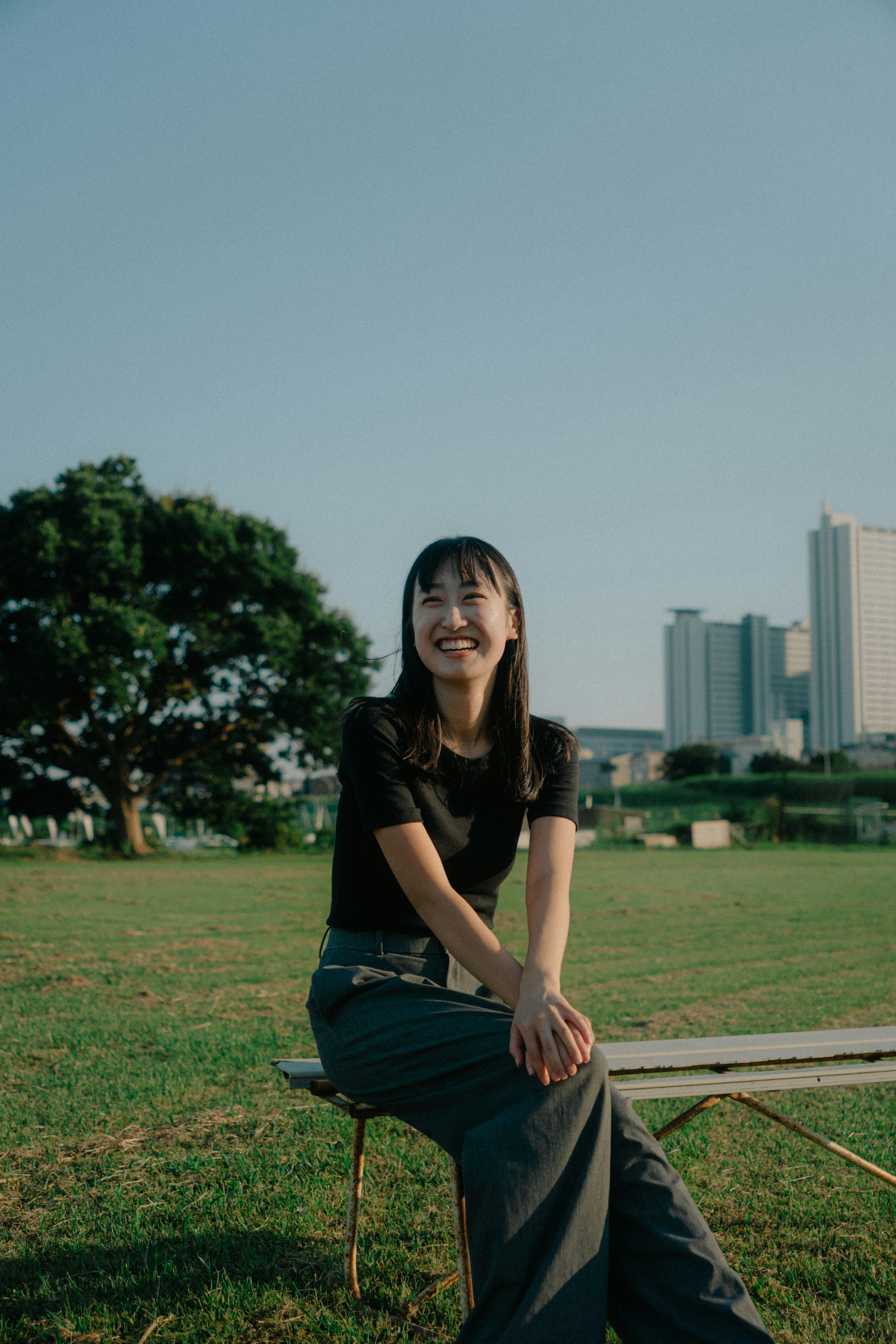 Mujer sonriente sentada en un parque con edificios y un árbol de fondo