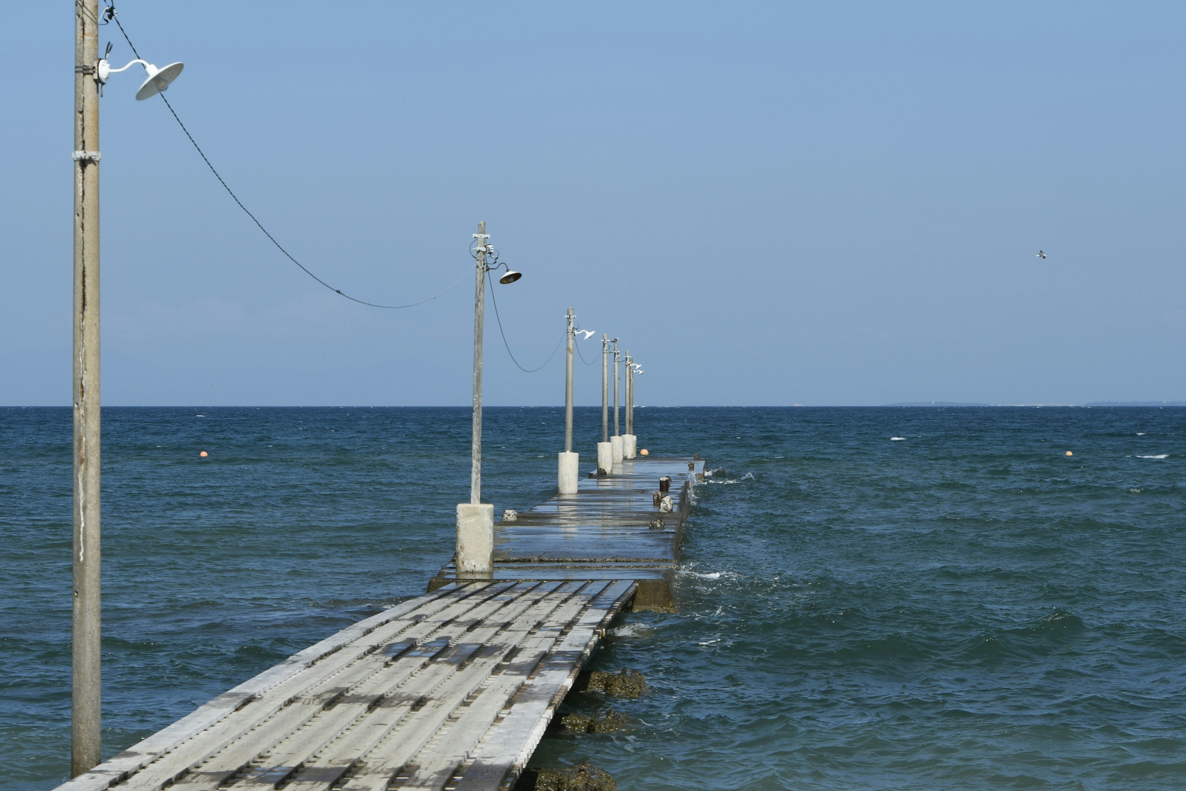 Holzsteg, der in das wellige Meer unter einem klaren blauen Himmel führt