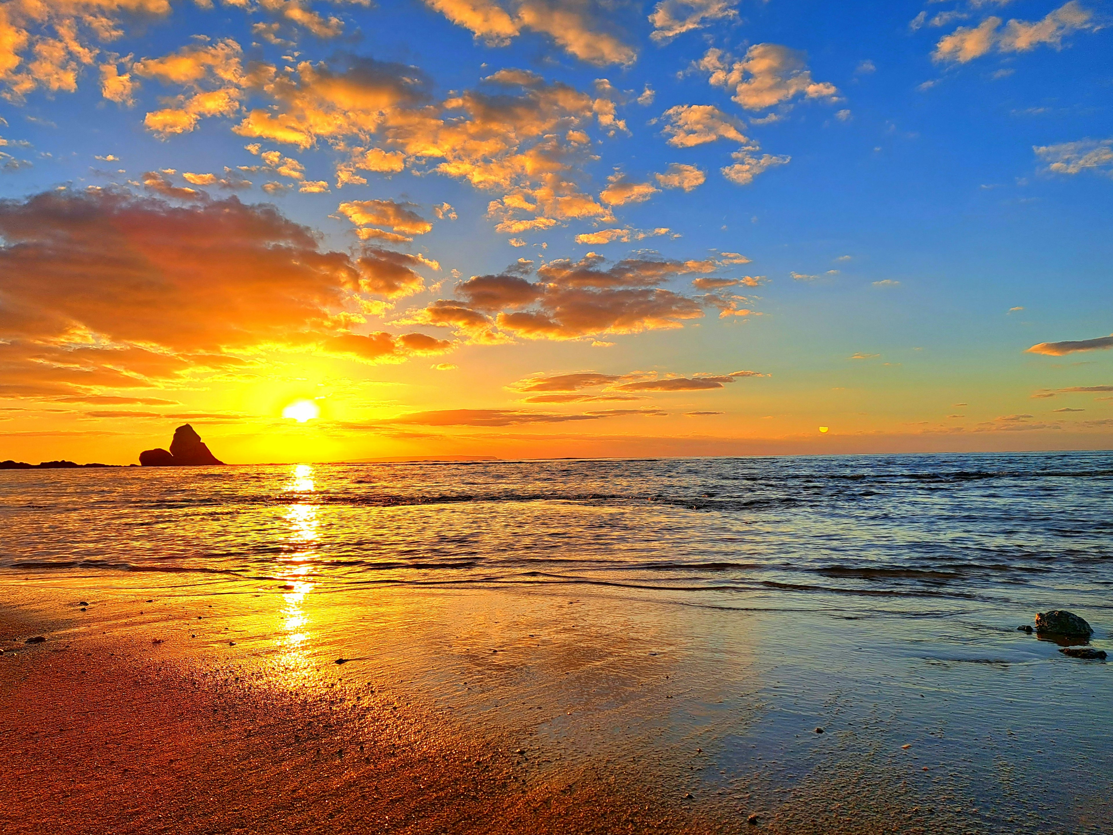 Pemandangan pantai yang indah dengan matahari terbenam di atas lautan ombak dan pasir bersinar