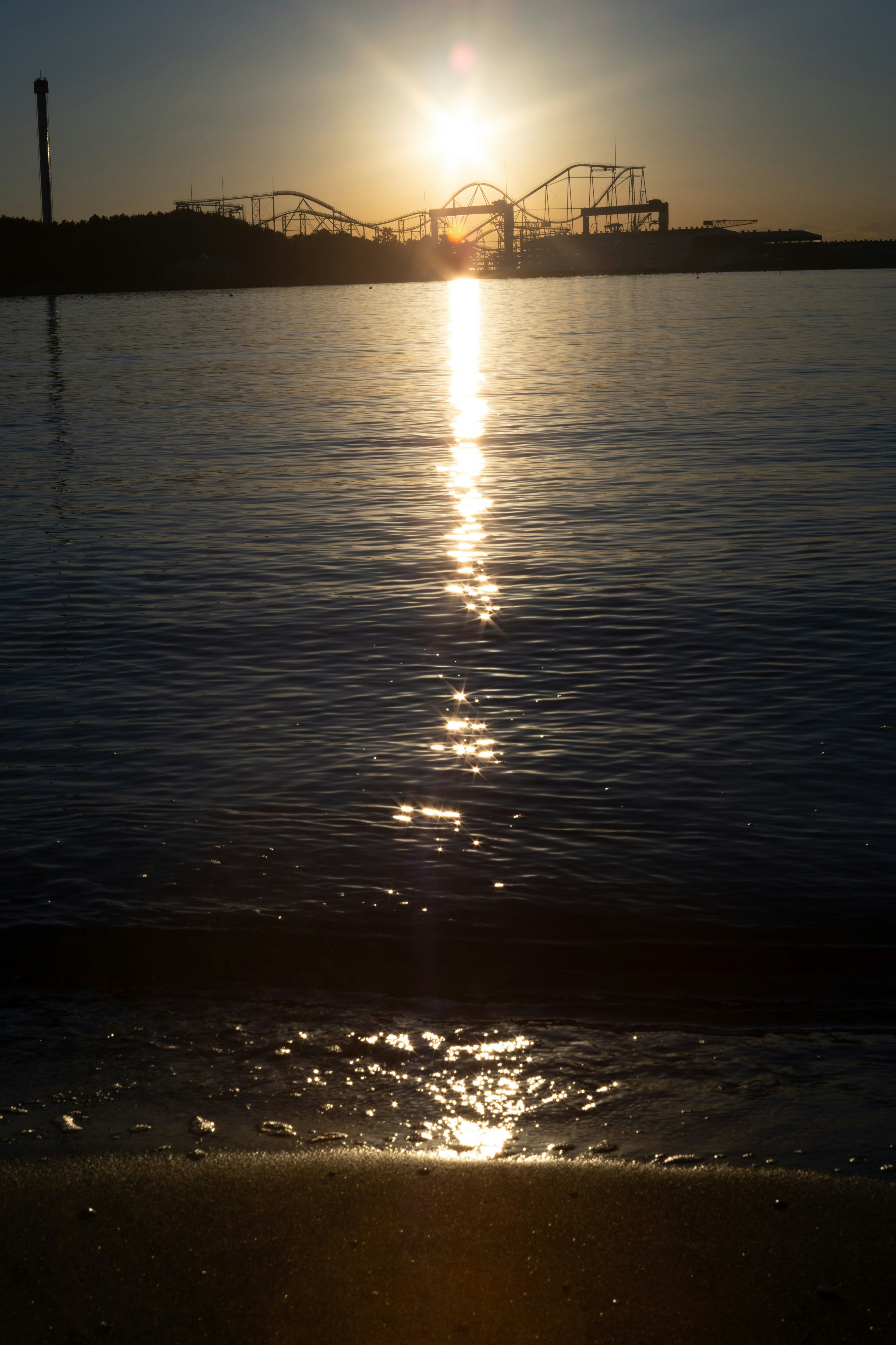 海の反射と遊園地のシルエットを背景にした夕日