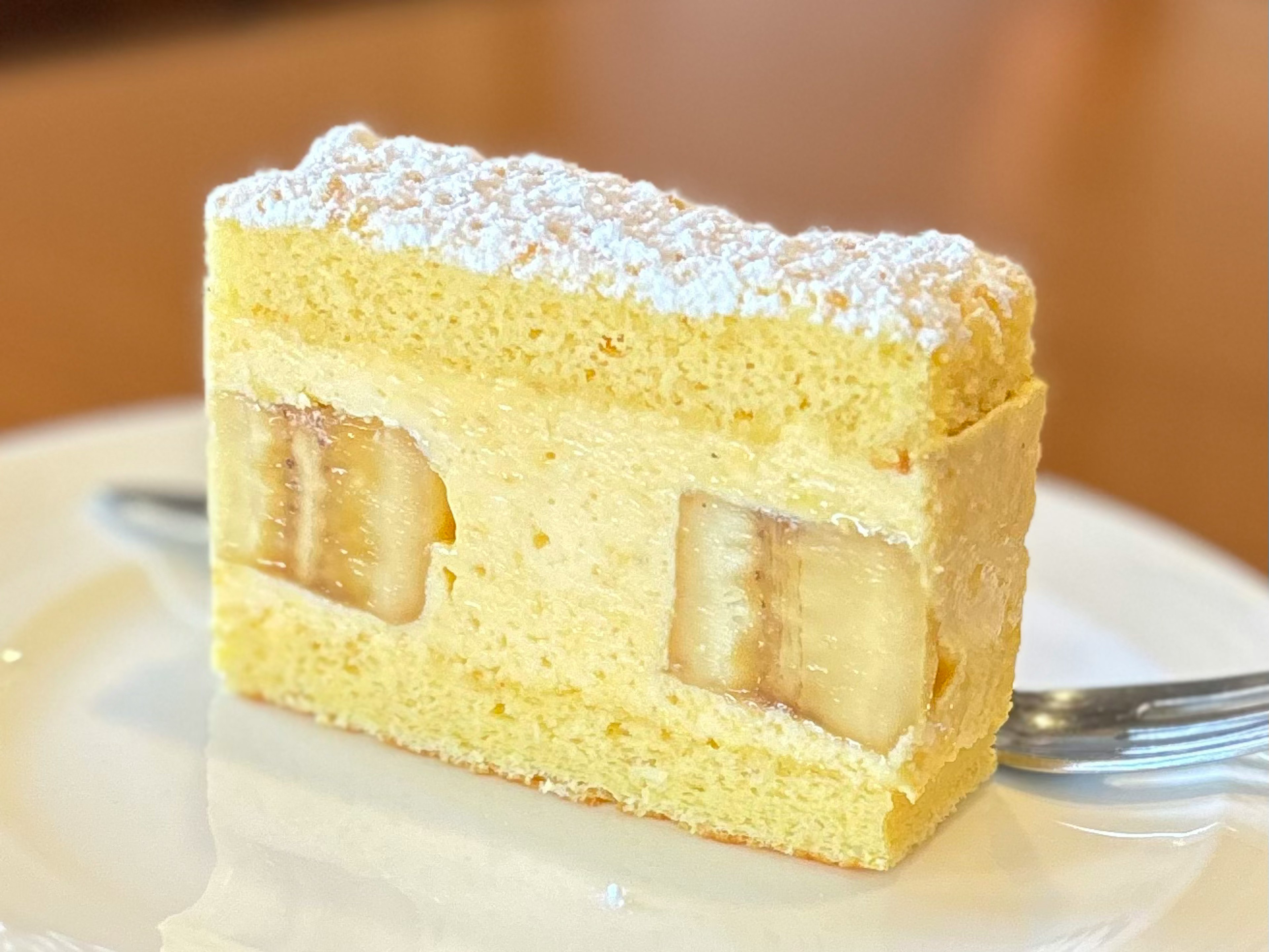 Slice of cream cake with banana filling yellow sponge cake topped with powdered sugar