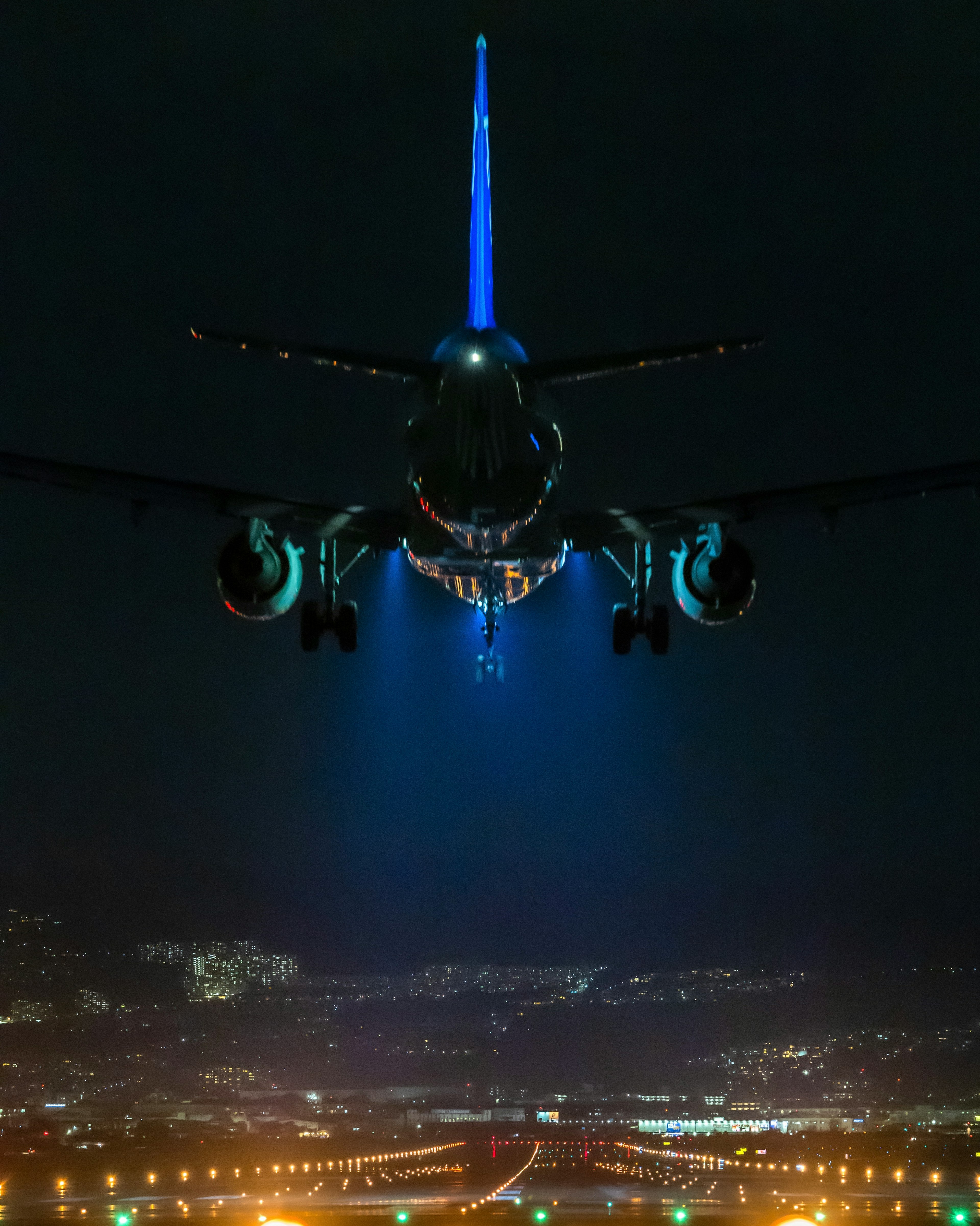 Vista posteriore di un aereo che vola di notte con luci della città sottostanti