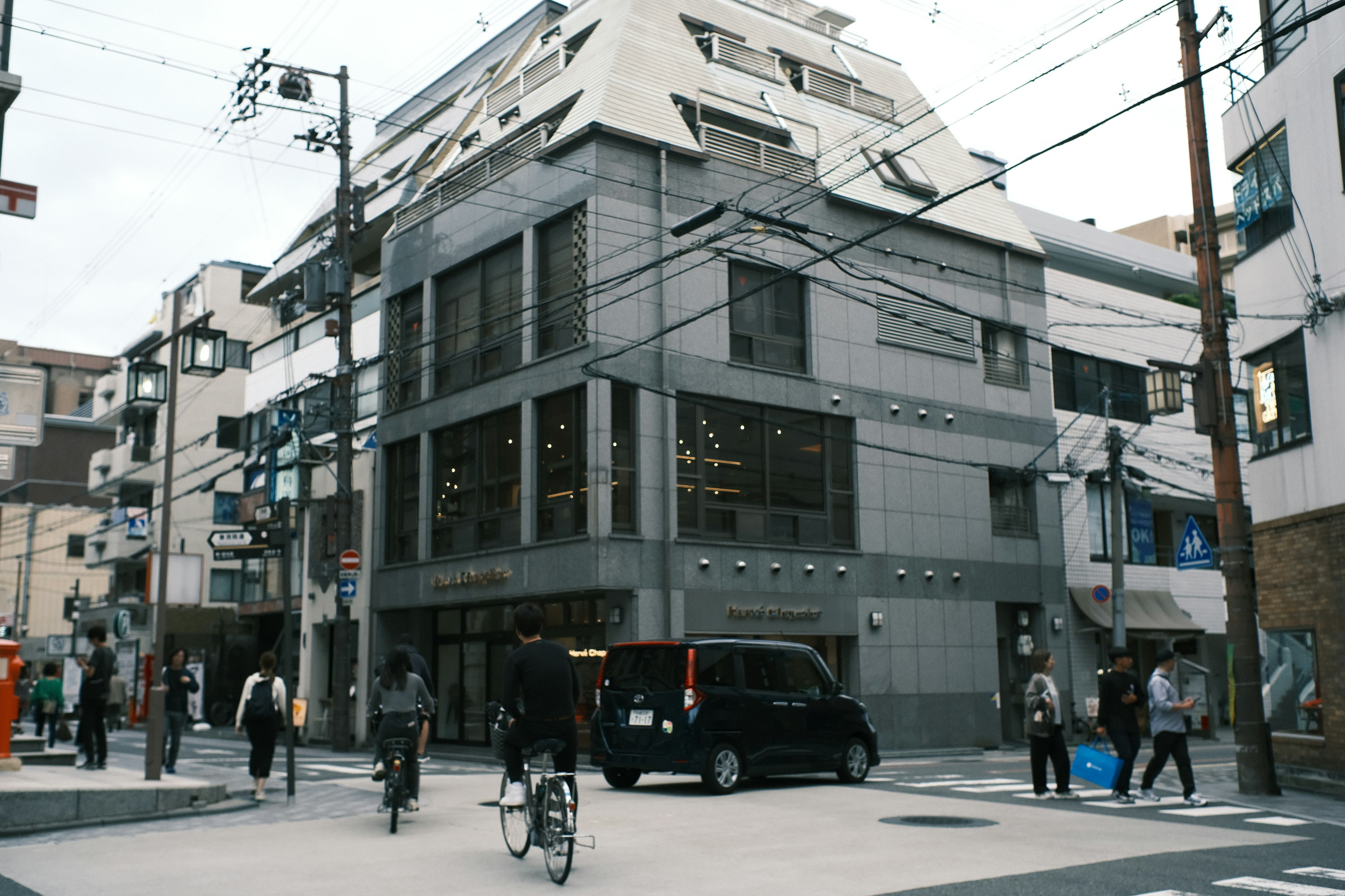 Edificio gris moderno en una intersección con personas caminando y en bicicleta