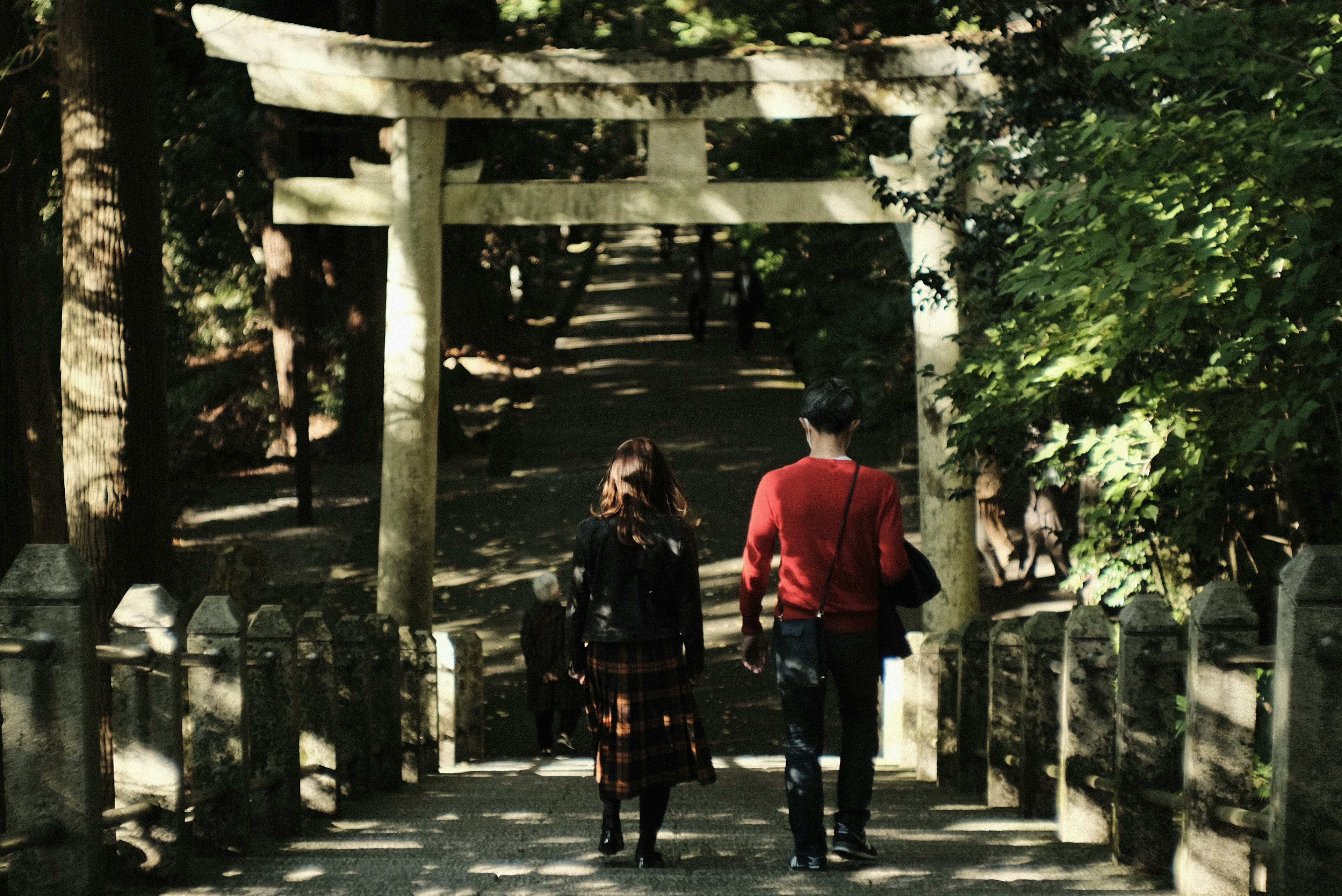 二人の人物が鳥居の下を歩いている森の中の風景