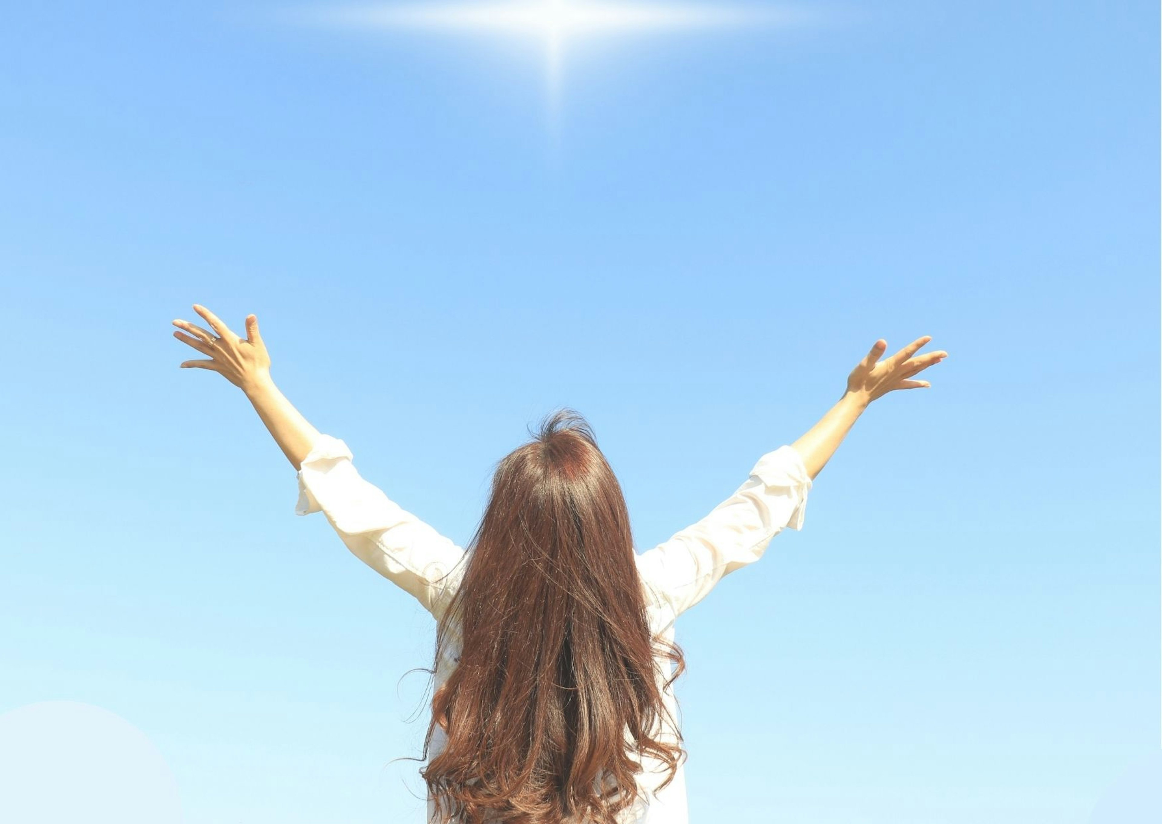 Une femme aux longs cheveux étendant les bras sous un ciel bleu lumineux