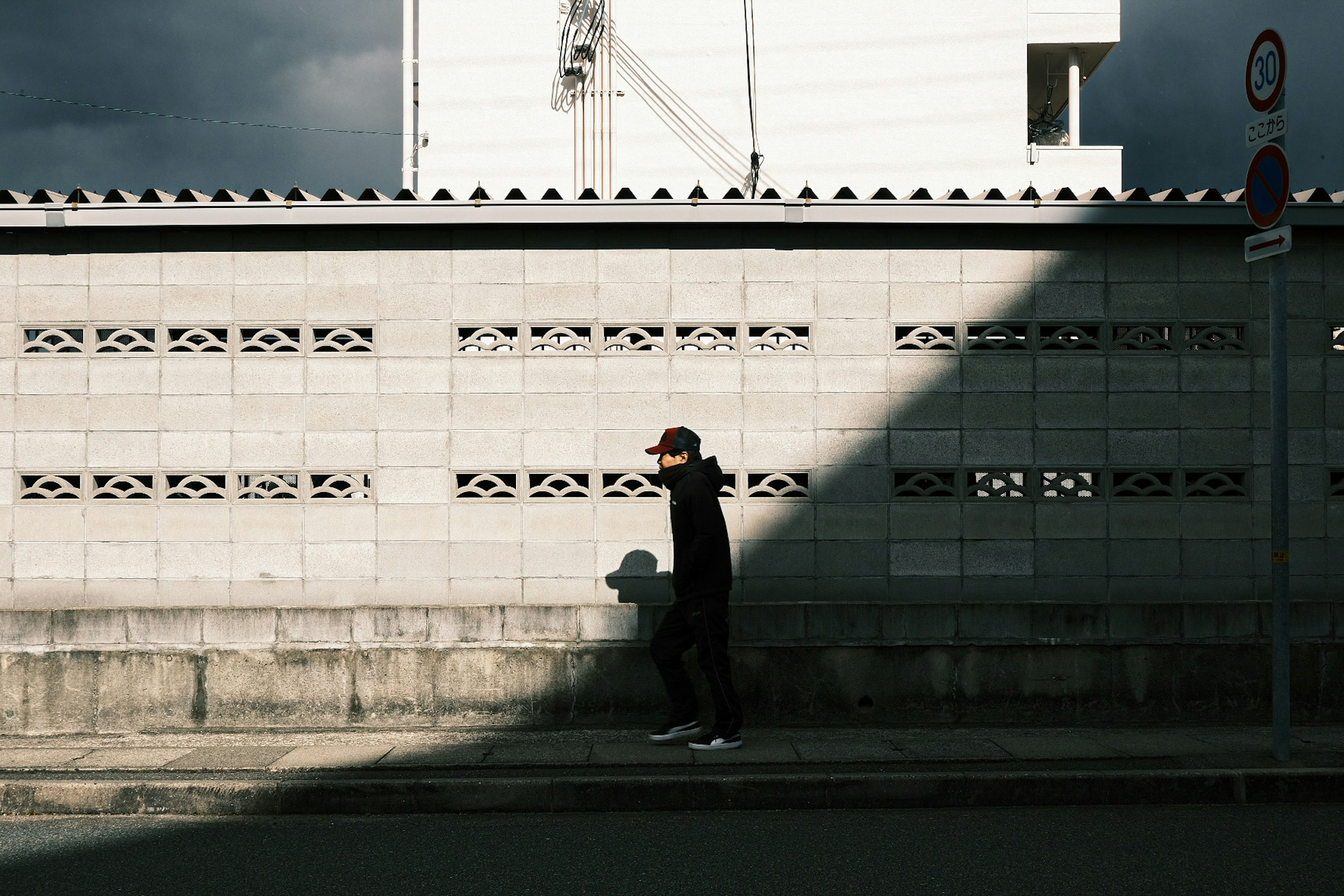 A person walking in shadow beside a concrete wall