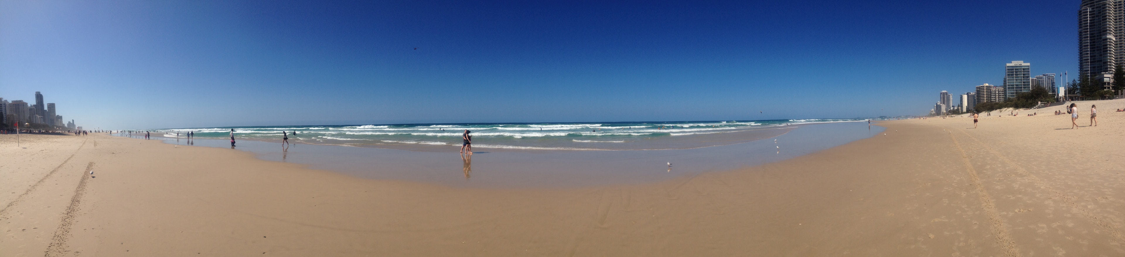 ภาพพาโนรามาของชายหาดที่มีท้องฟ้าสีฟ้าและคลื่น