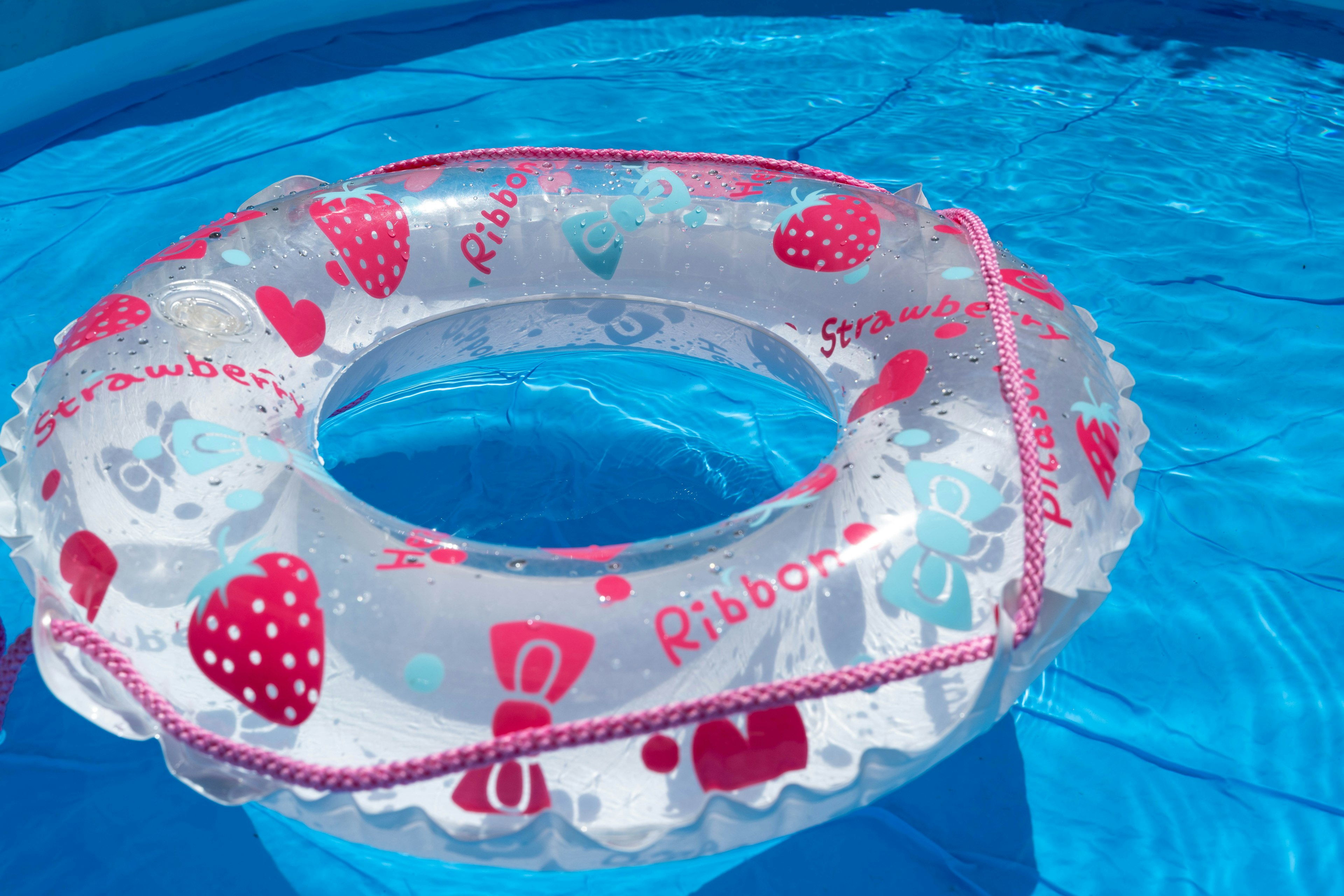 A strawberry-patterned inflatable ring floating in a pool