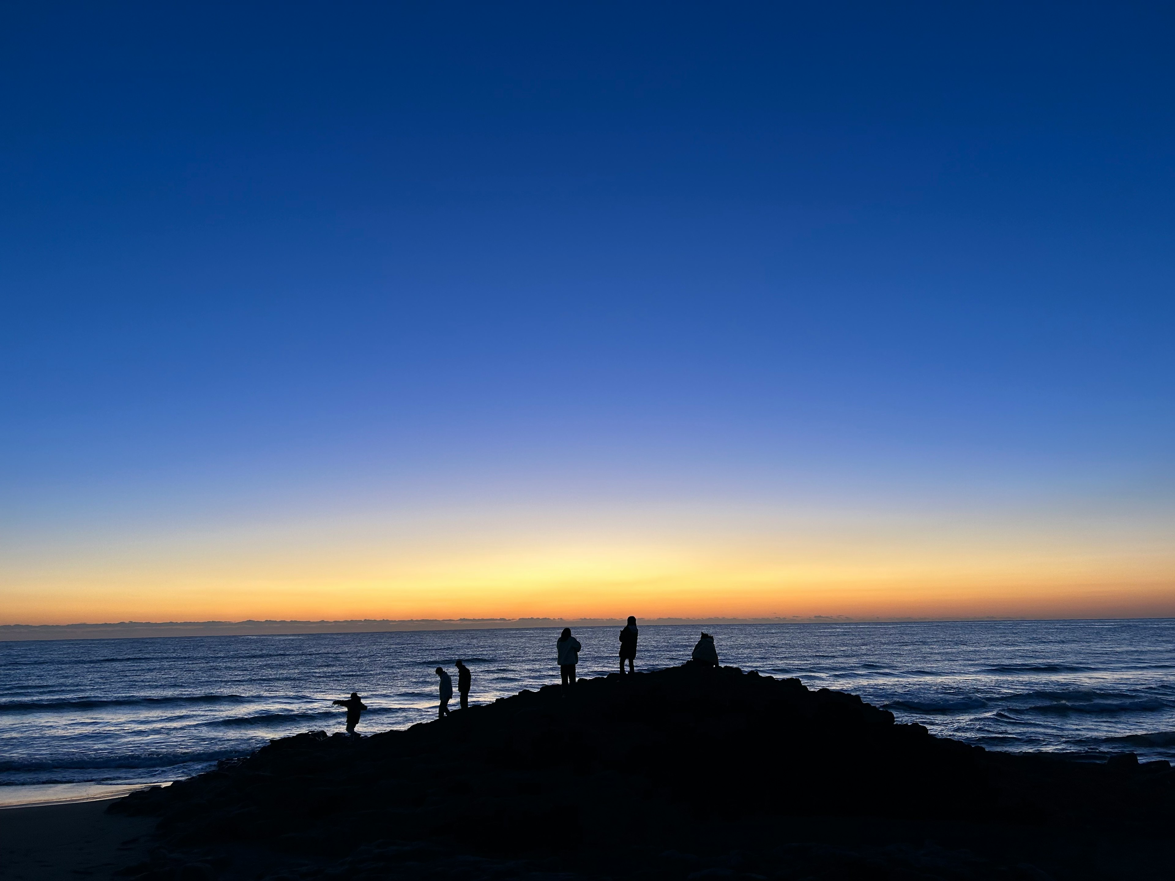 Silhouette di persone su una spiaggia rocciosa al tramonto