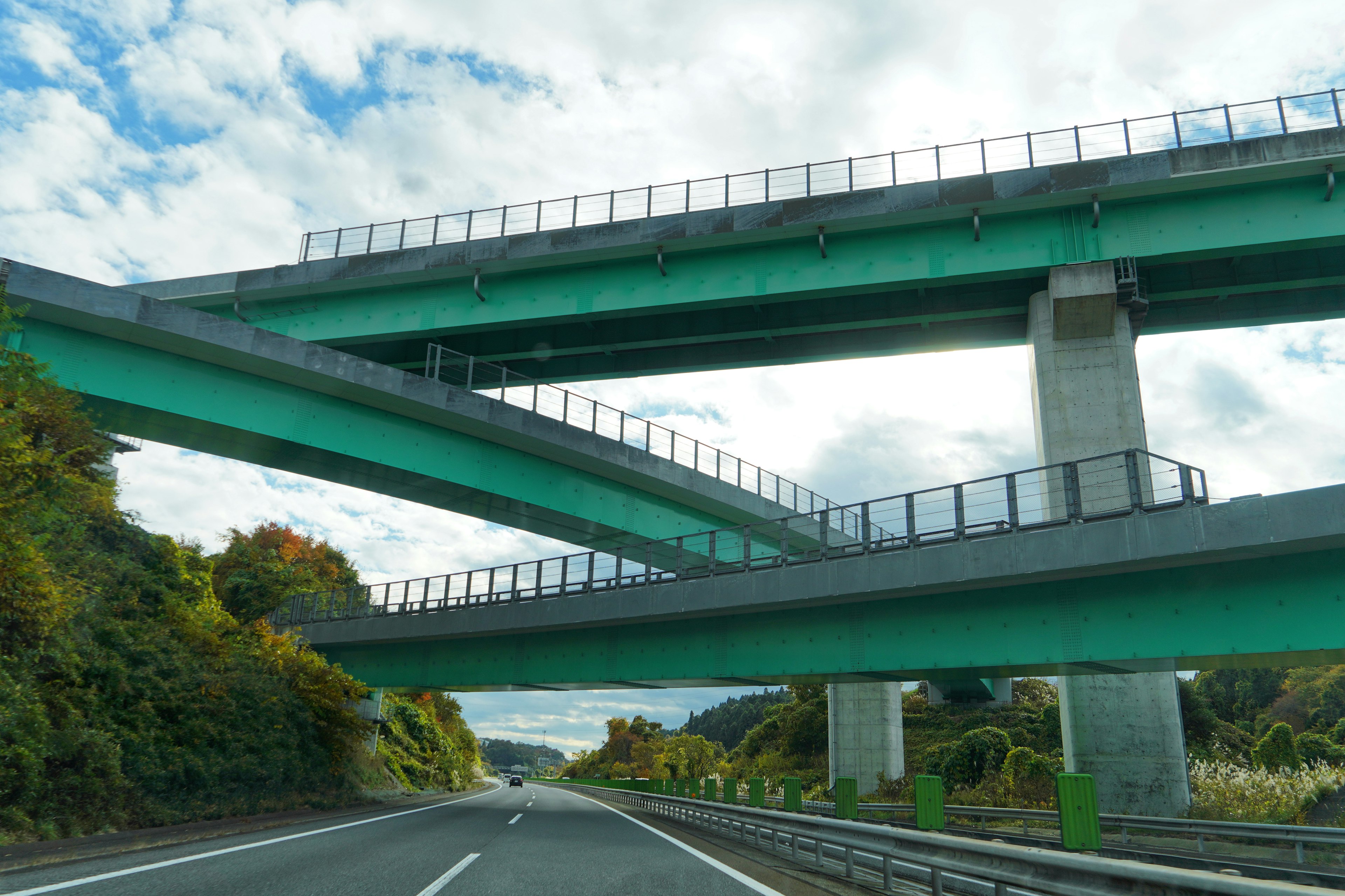 Intersecting green overpasses with a backdrop of blue sky and clouds