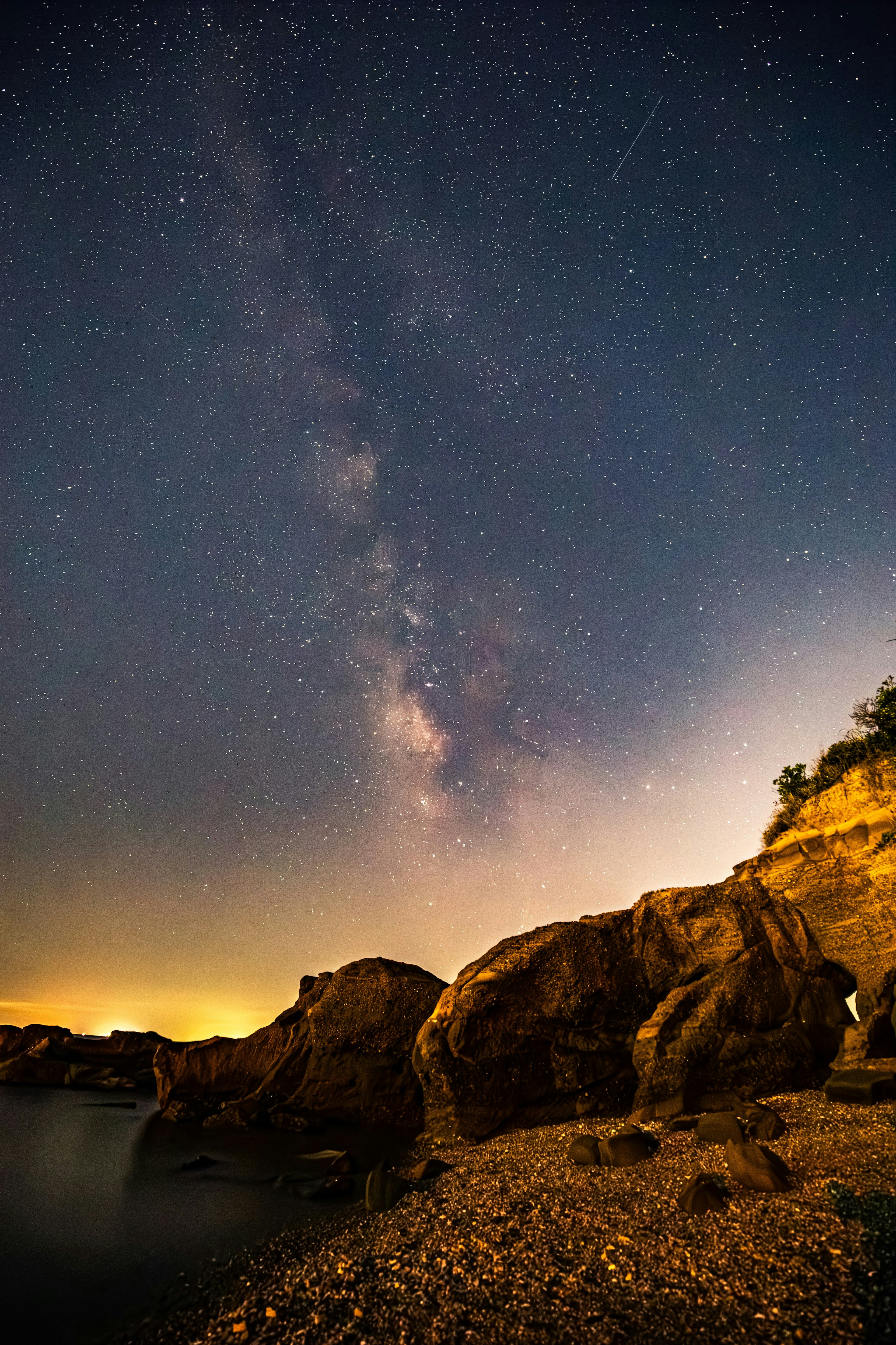 Vista panoramica di rocce vicino al mare sotto un cielo stellato con la Via Lattea